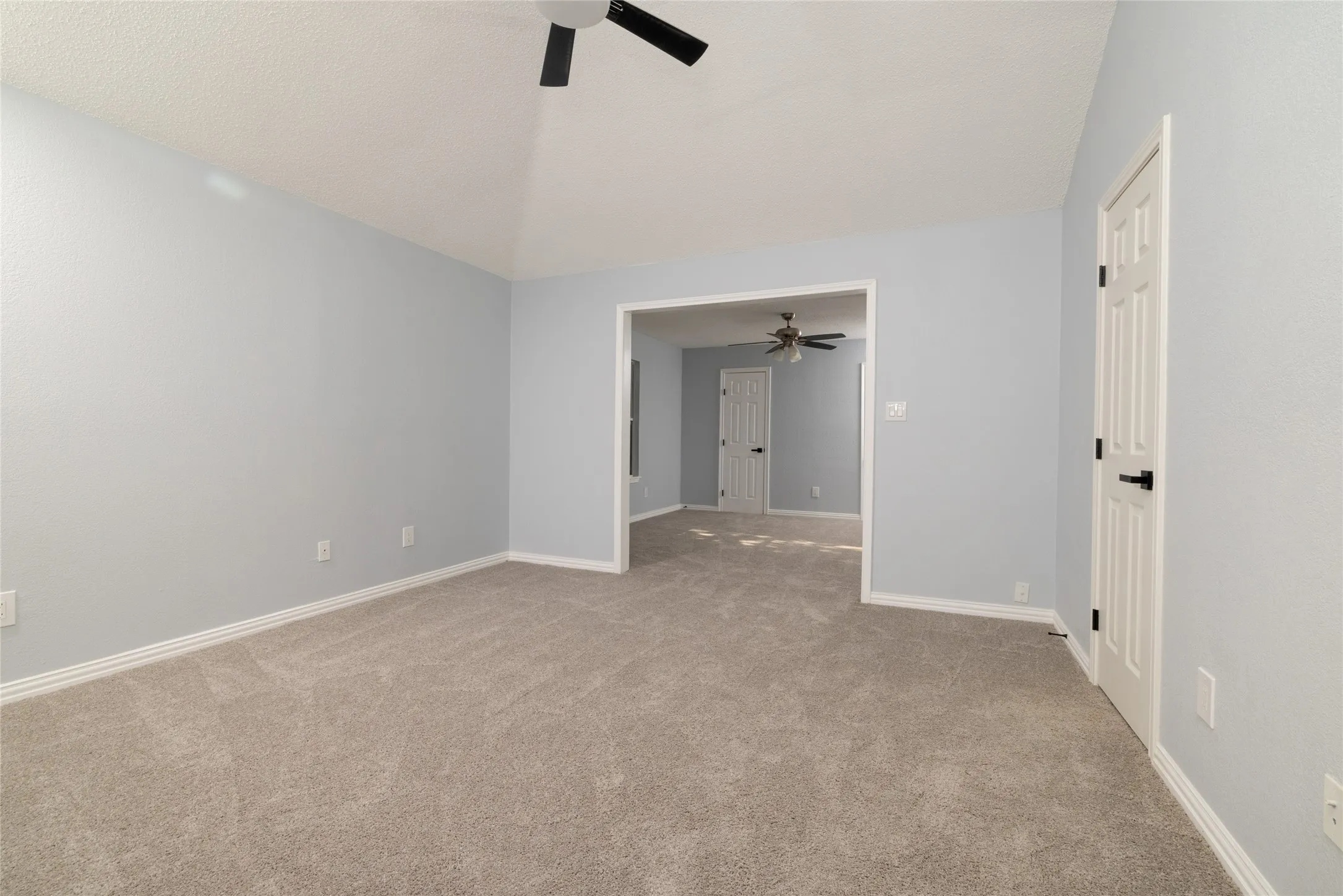 Vaulted ceiling with a ceiling fan, neutral wall paint, light-toned carpeting, and white paneled doors with black hardware