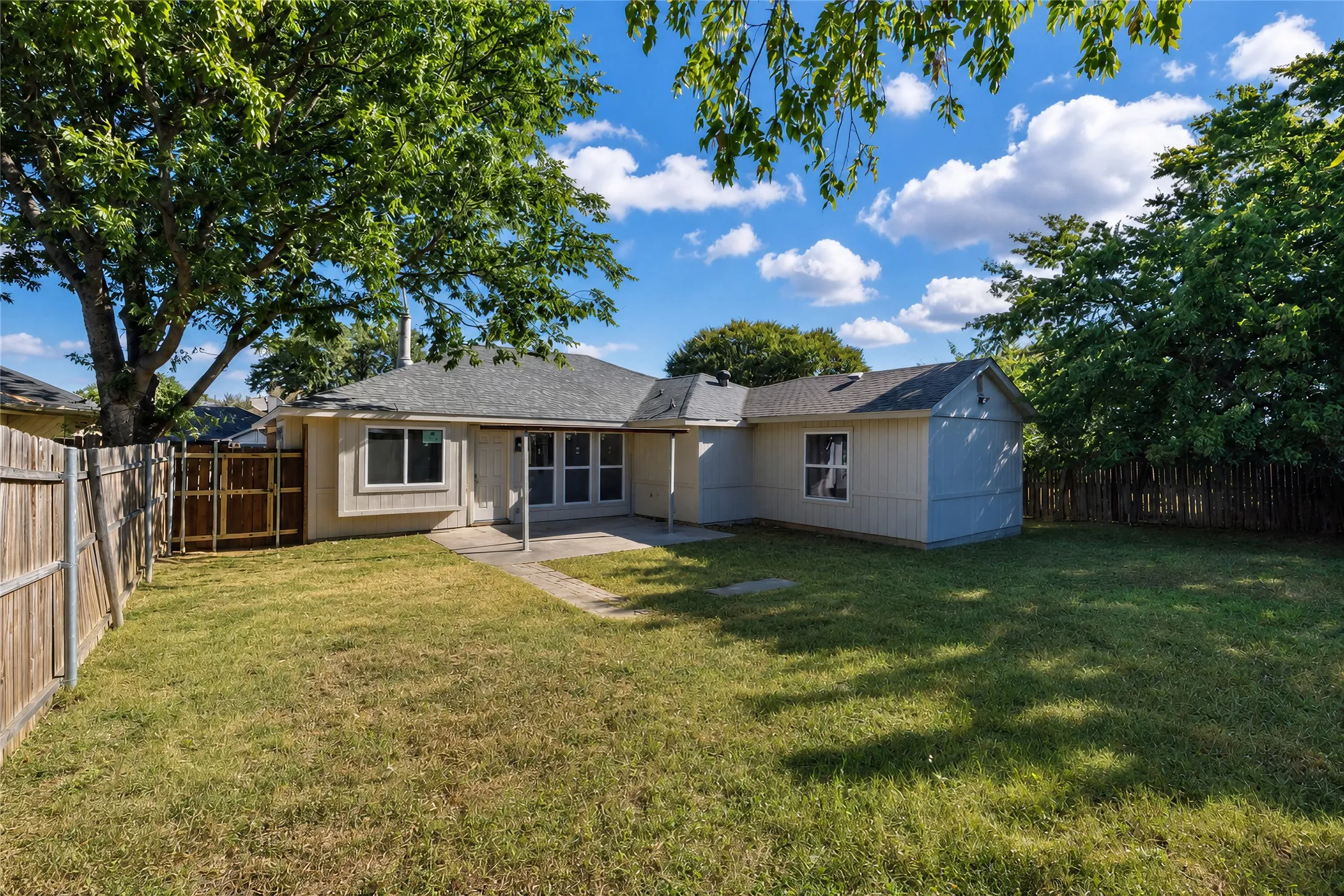 Expansive backyard featuring a manicured lawn, established trees, privacy fencing, and a concrete patio