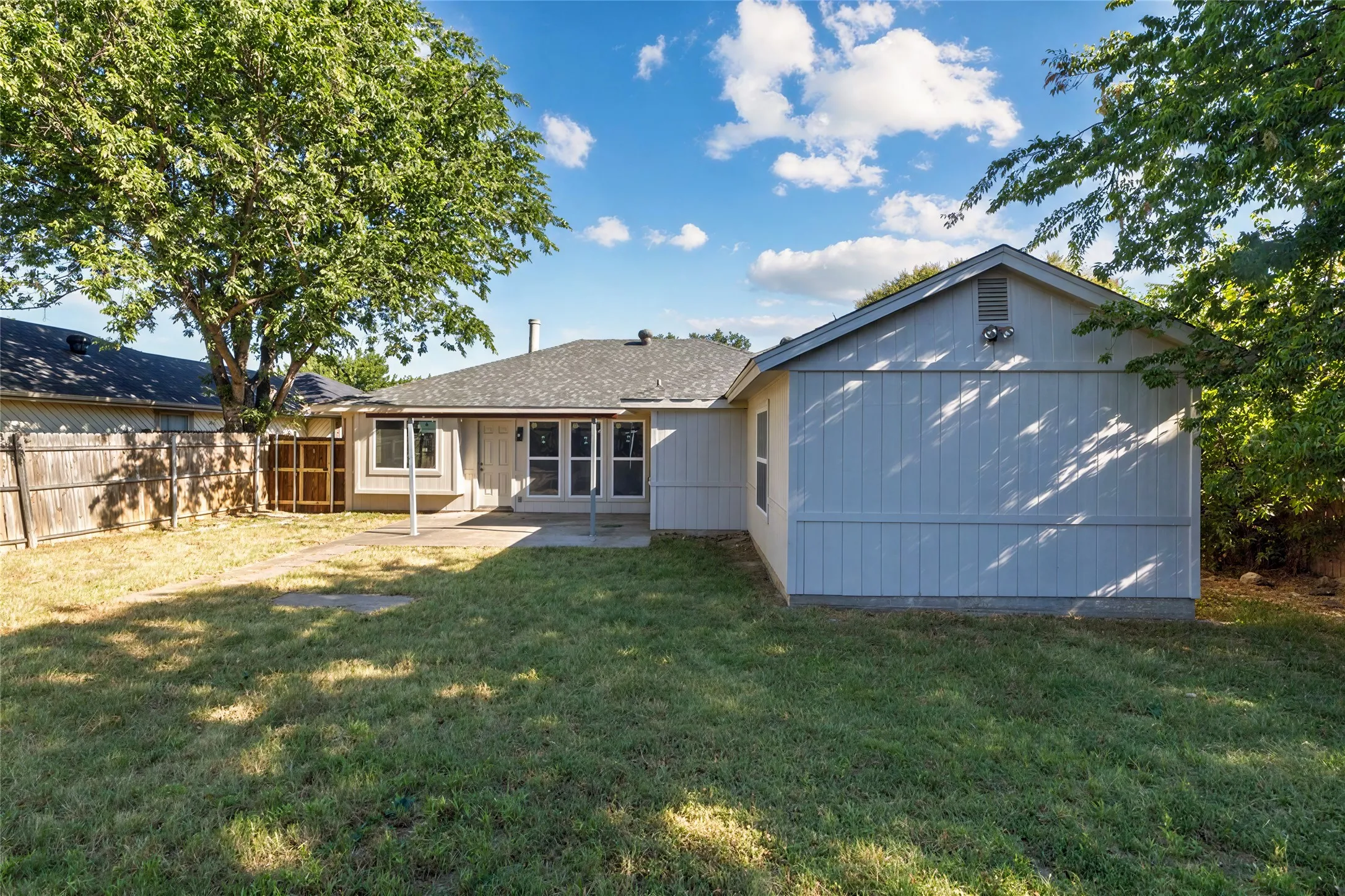 Expansive backyard featuring a concrete patio, mature trees, and a wood privacy fence