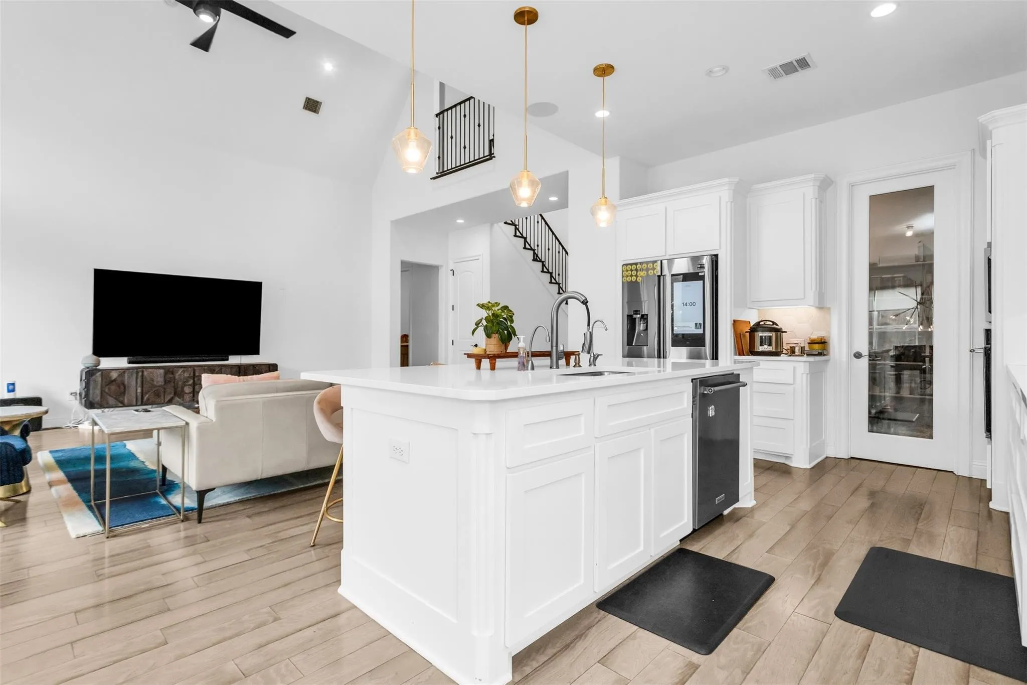 High ceilings, wood-finish flooring, white cabinetry, kitchen island with sink, and contemporary pendant lighting