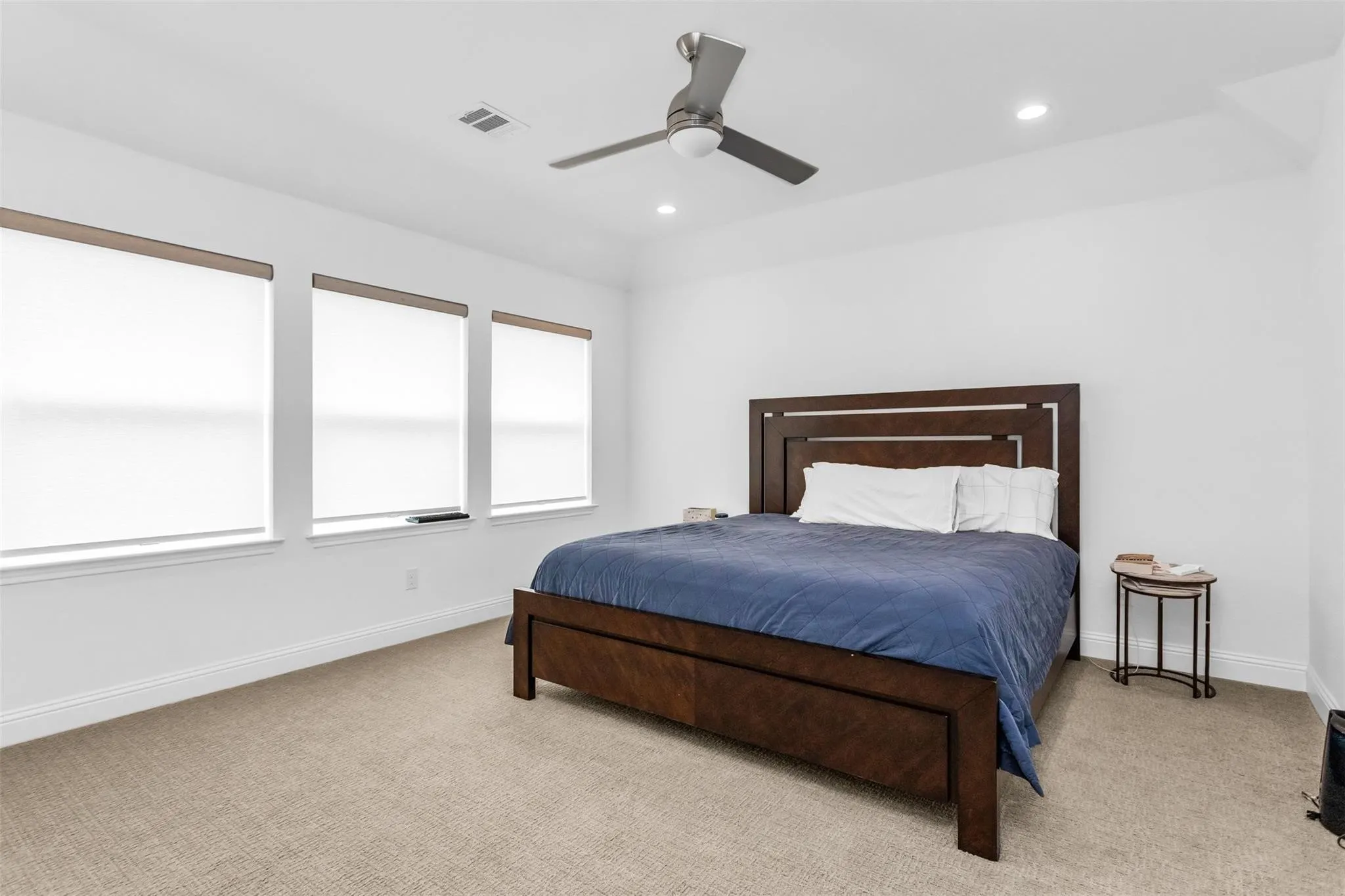 Recessed lighting, ceiling fan, three windows with roller shades, and light-toned carpeting