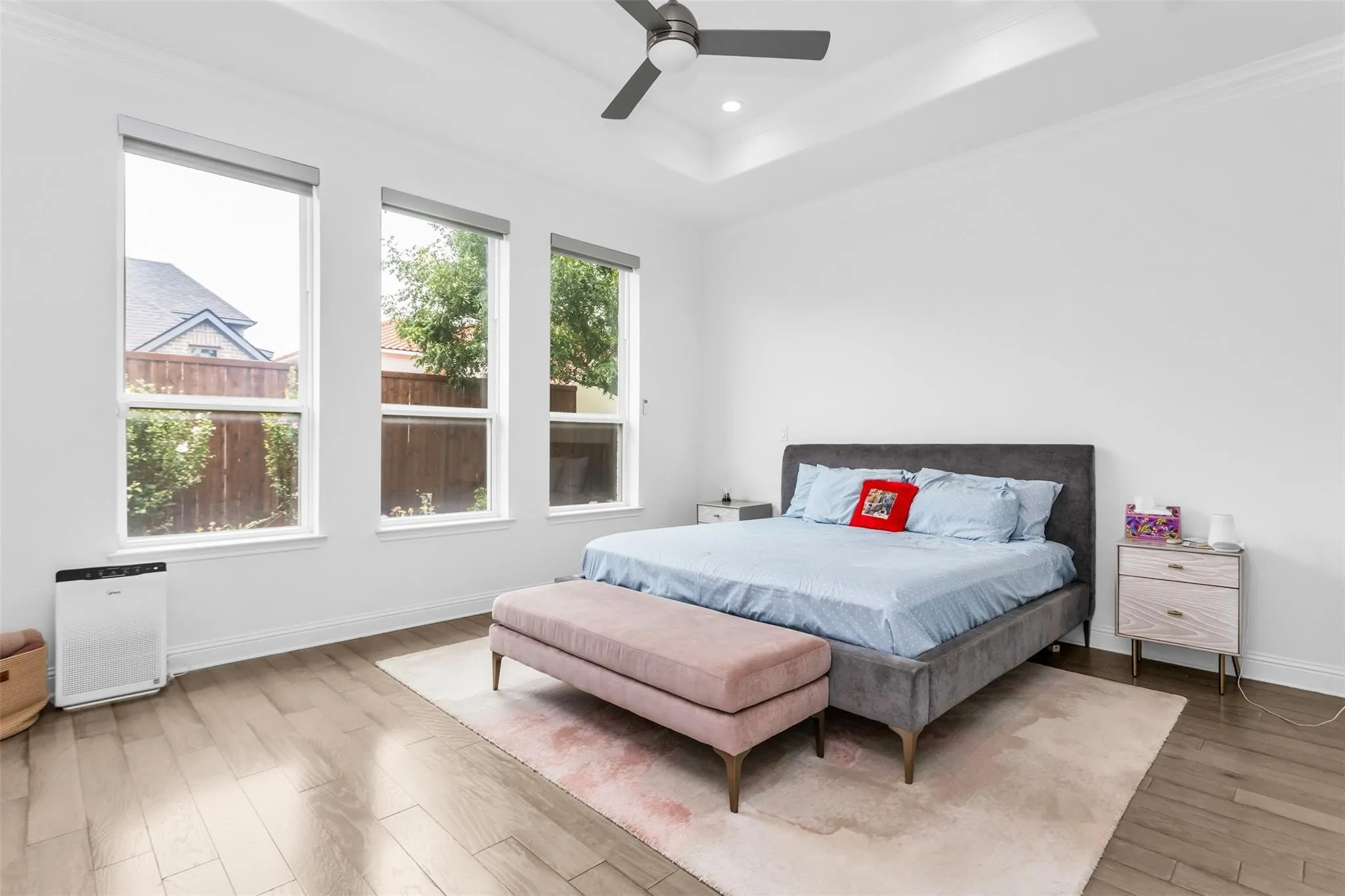 Tray ceiling with recessed lighting, wood-finish flooring, three tall windows, ceiling fan, and white walls