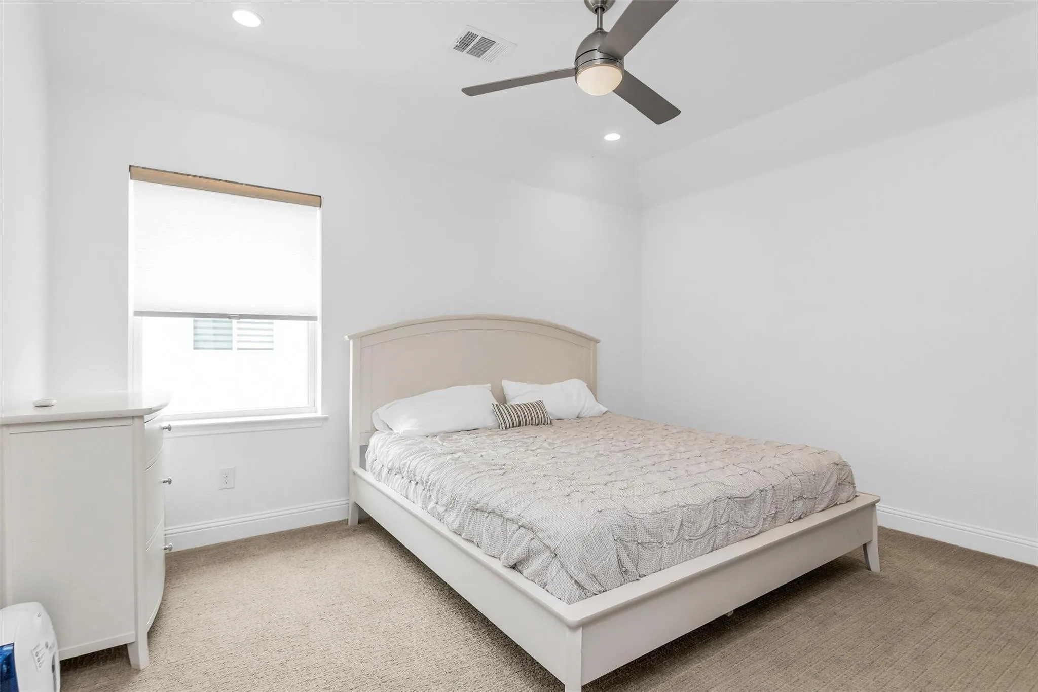 Recessed lighting, window with roller shade, ceiling fan with integrated light, light-toned carpeting, and a white color palette
