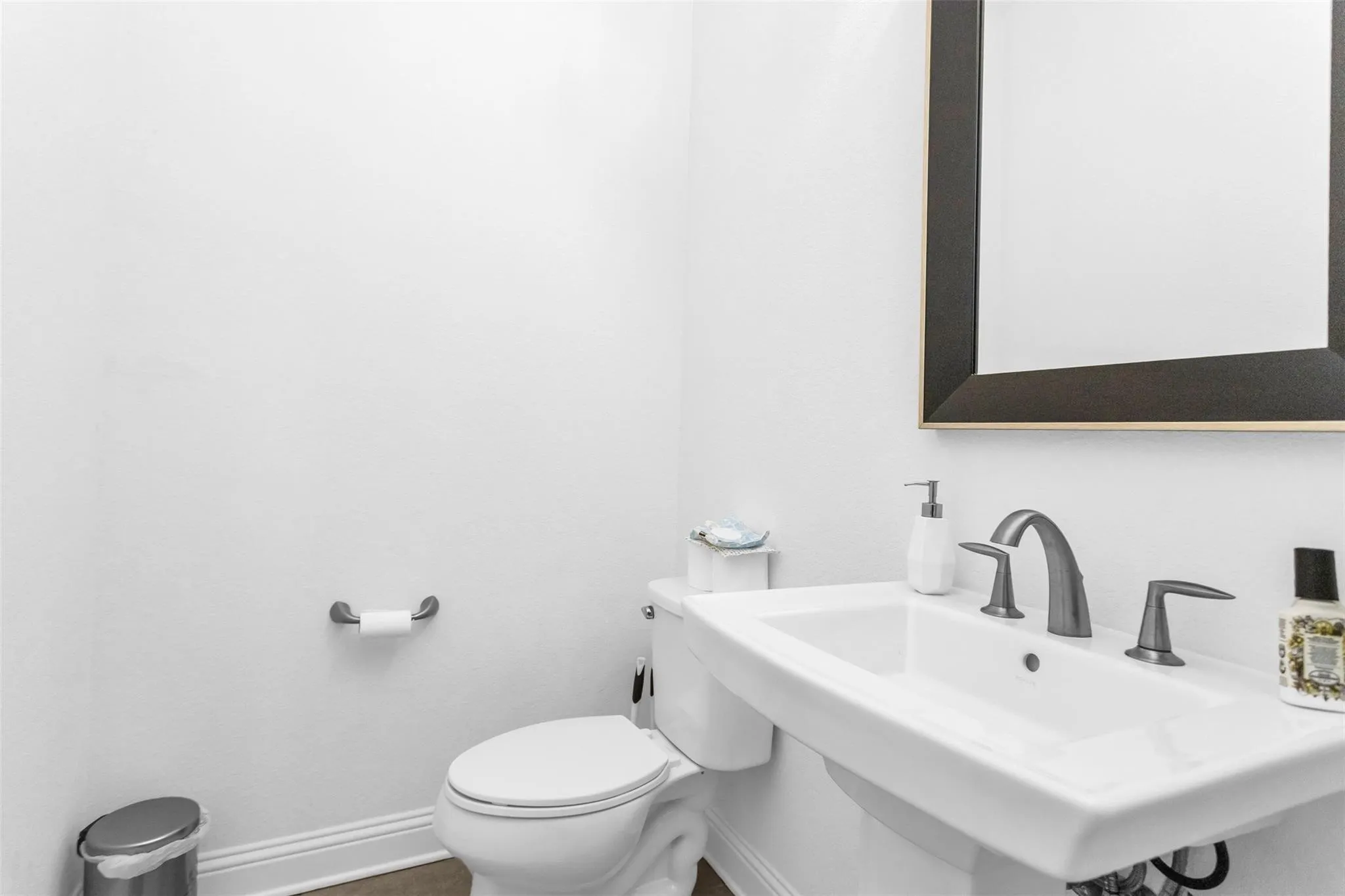 Pedestal sink with a wide basin, three-piece faucet, and a framed mirror