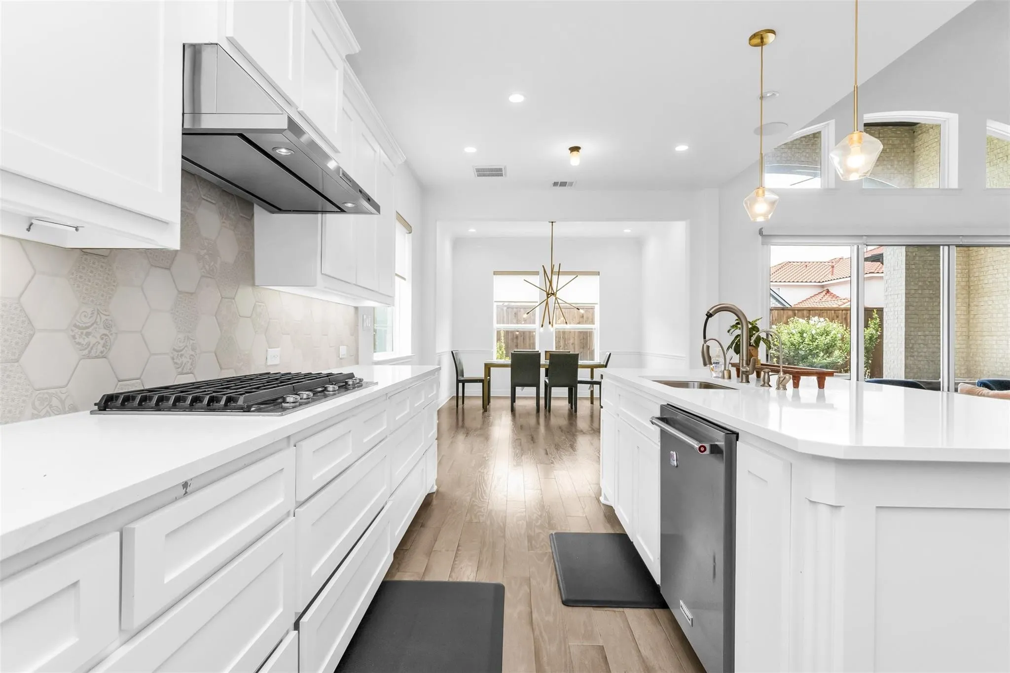White cabinetry with paneling, stainless steel appliances, hexagon tile backsplash, wood-finish flooring, and pendant lighting
