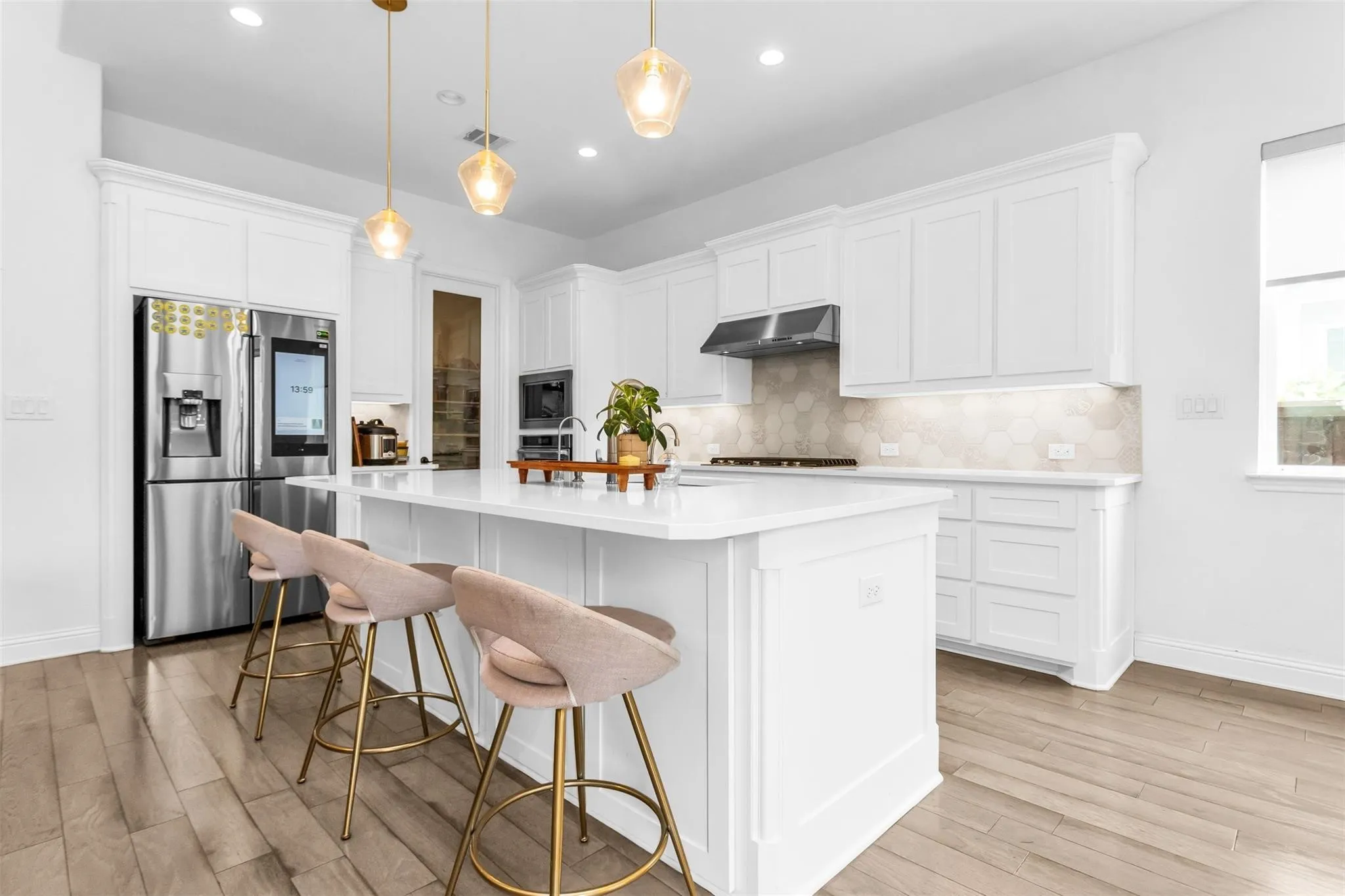 Spacious kitchen with a central island, white cabinetry, hexagon tile backsplash, stainless steel appliances, and wood-finish flooring