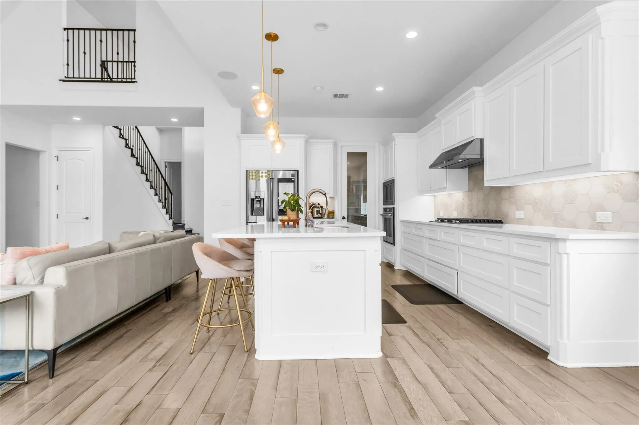 Open-concept kitchen featuring an expansive island, white cabinetry, integrated stainless steel appliances, and a hexagon tile backsplash