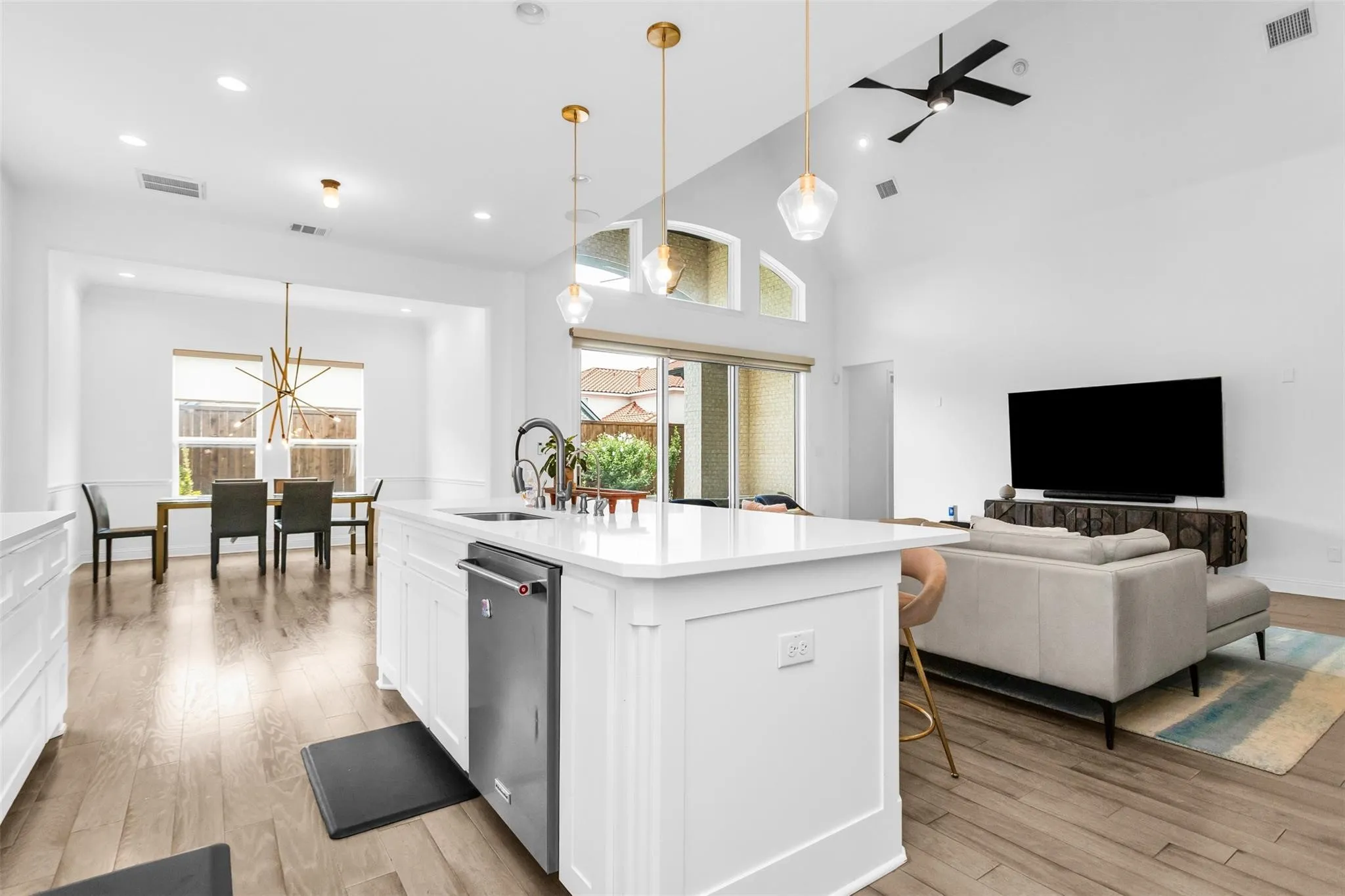 Open-concept living space featuring wood-finish flooring, a kitchen island with integrated dishwasher, high vaulted ceilings, and a modern ceiling fan