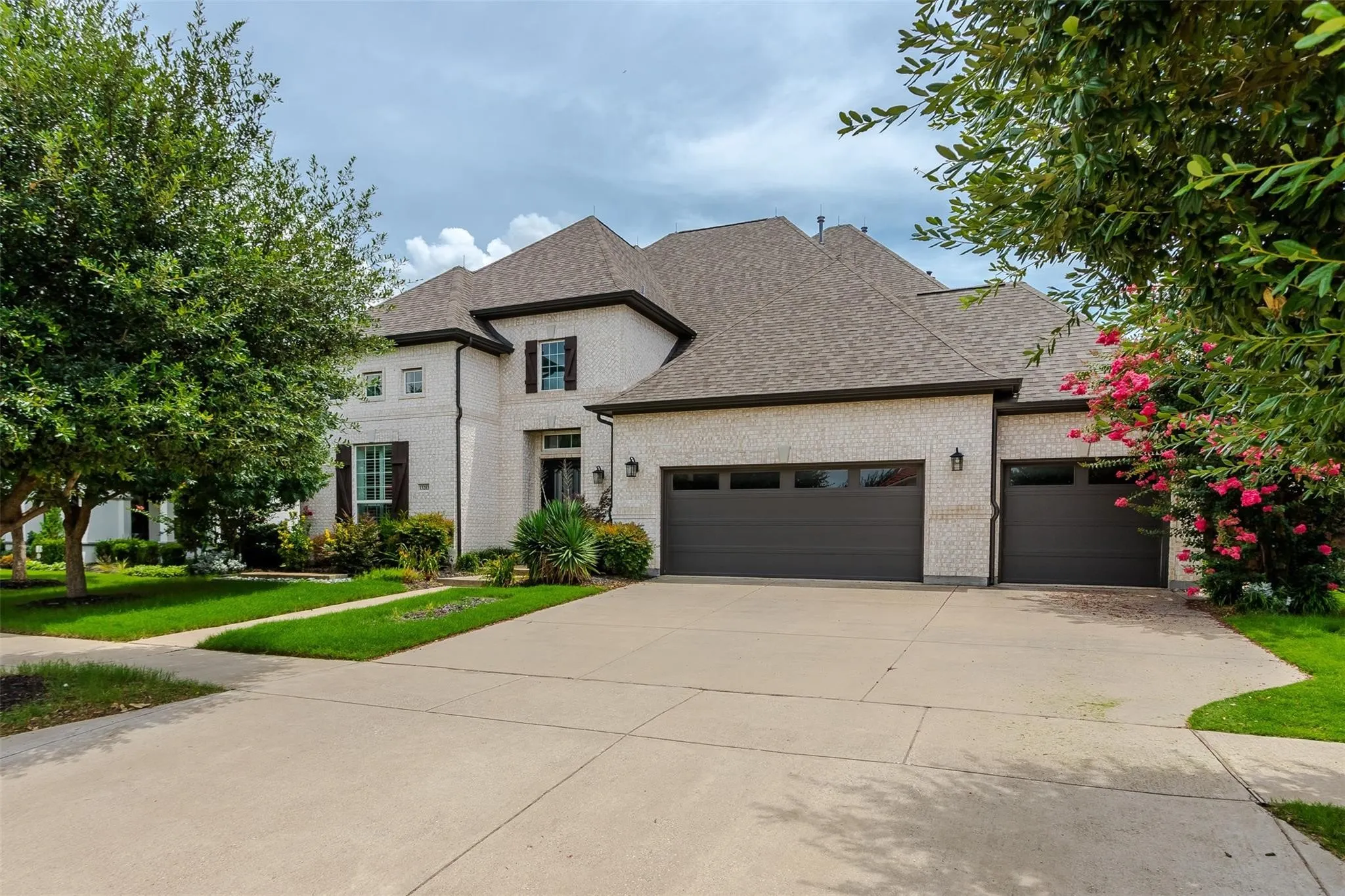 Stucco exterior with dark trim accents, multi-car garage, concrete driveway, and established front landscaping