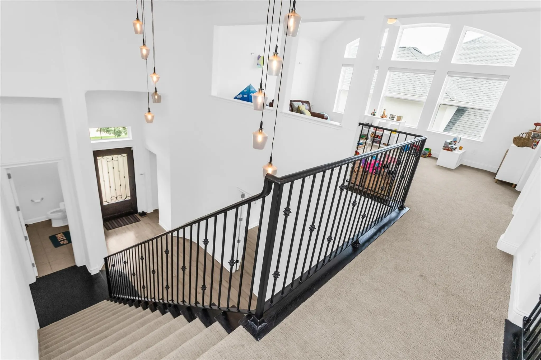 Two-story entry with multiple pendant lighting fixtures, wood-finish flooring, and a wrought iron staircase