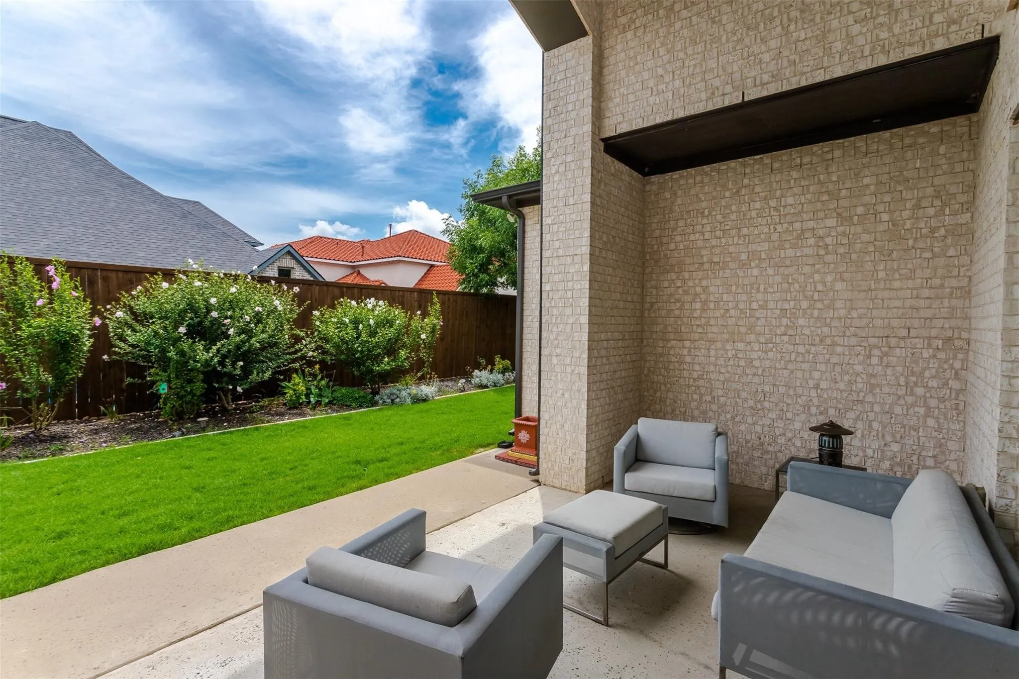 Covered patio with light-toned brick wall, concrete flooring, and a wooden privacy fence