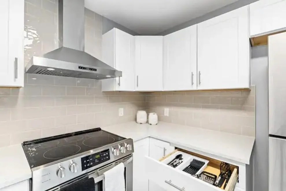 Stainless steel range with sleek hood, white shaker cabinets, and light-toned tile backsplash