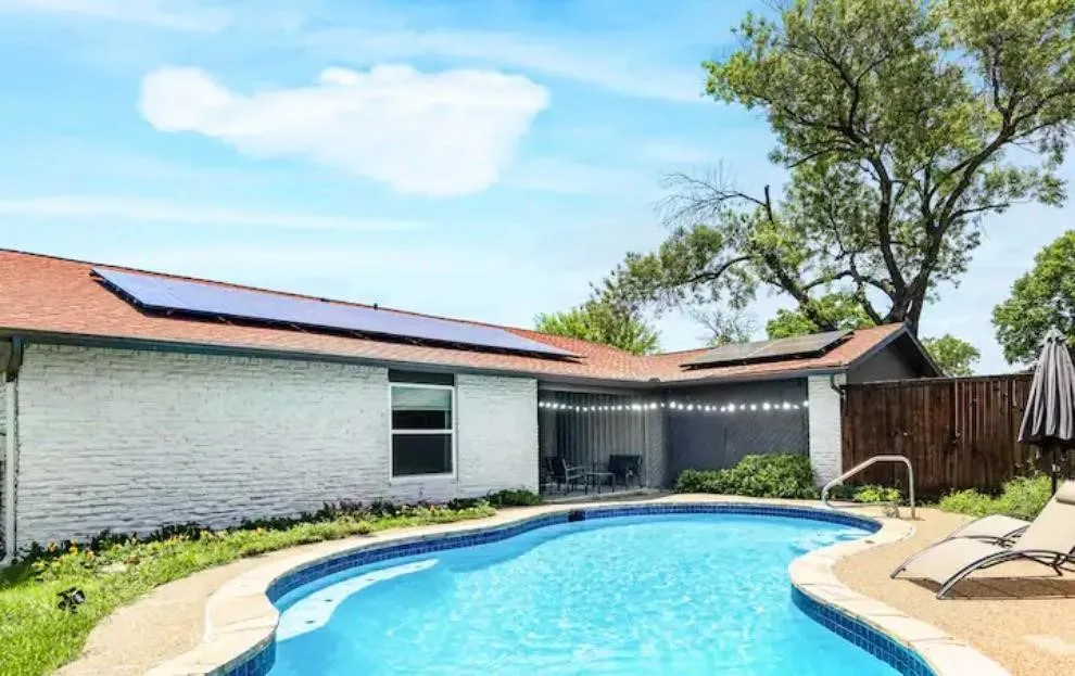 In-ground swimming pool with a curved design, white brick exterior, and an attached covered patio
