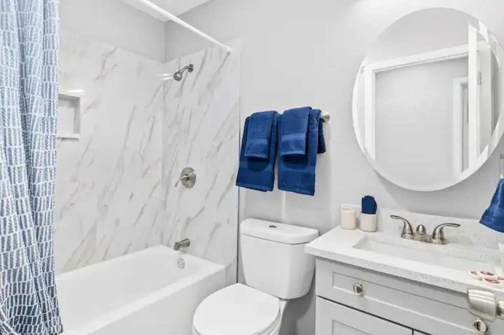 Bathroom featuring a white tub, built-in shower niche, and a vanity with an integrated sink and round mirror