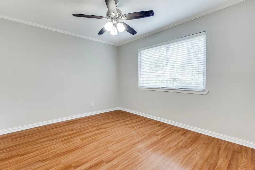Wood-finish flooring, ceiling fan with integrated lighting, window with blinds, and crown molding