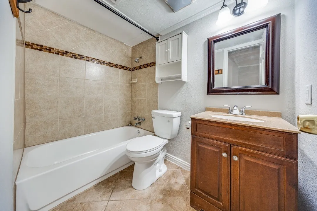 Tiled shower surround with mosaic accent, wood vanity with integrated sink, framed mirror, and wall-mounted storage cabinet