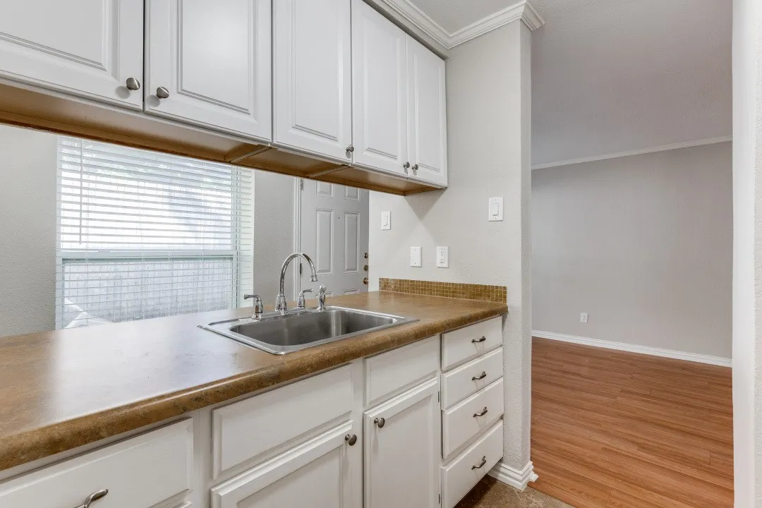 White upper and lower cabinetry, stainless steel sink with a chrome faucet, and wood-finish flooring
