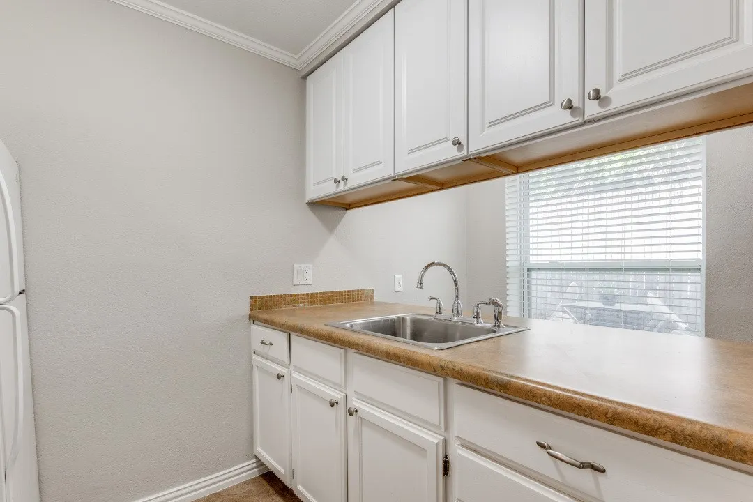 White shaker-style cabinetry, double basin stainless steel sink, chrome gooseneck faucet, light-toned countertops, and crown molding