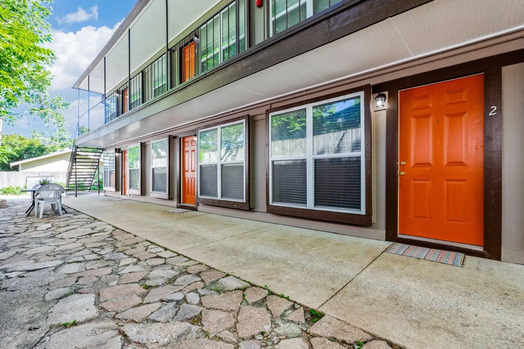 Ground-level entry with a stone patio, concrete walkway, and bright orange door