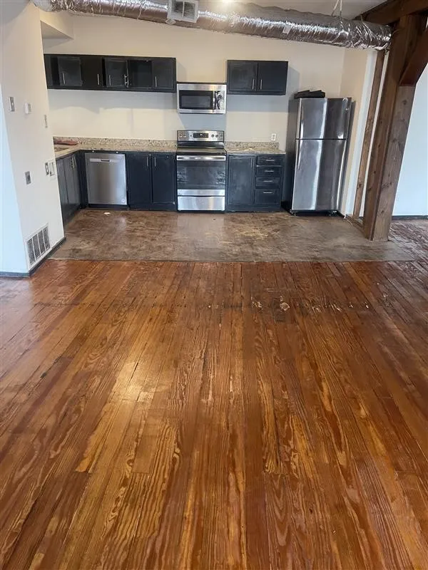 Wood-finish flooring throughout, kitchen with dark cabinetry, granite-style countertops, and stainless steel appliances