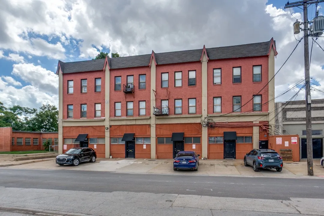 Brick facade with multiple windows, prominent gabled roofline, and ground-level entryways