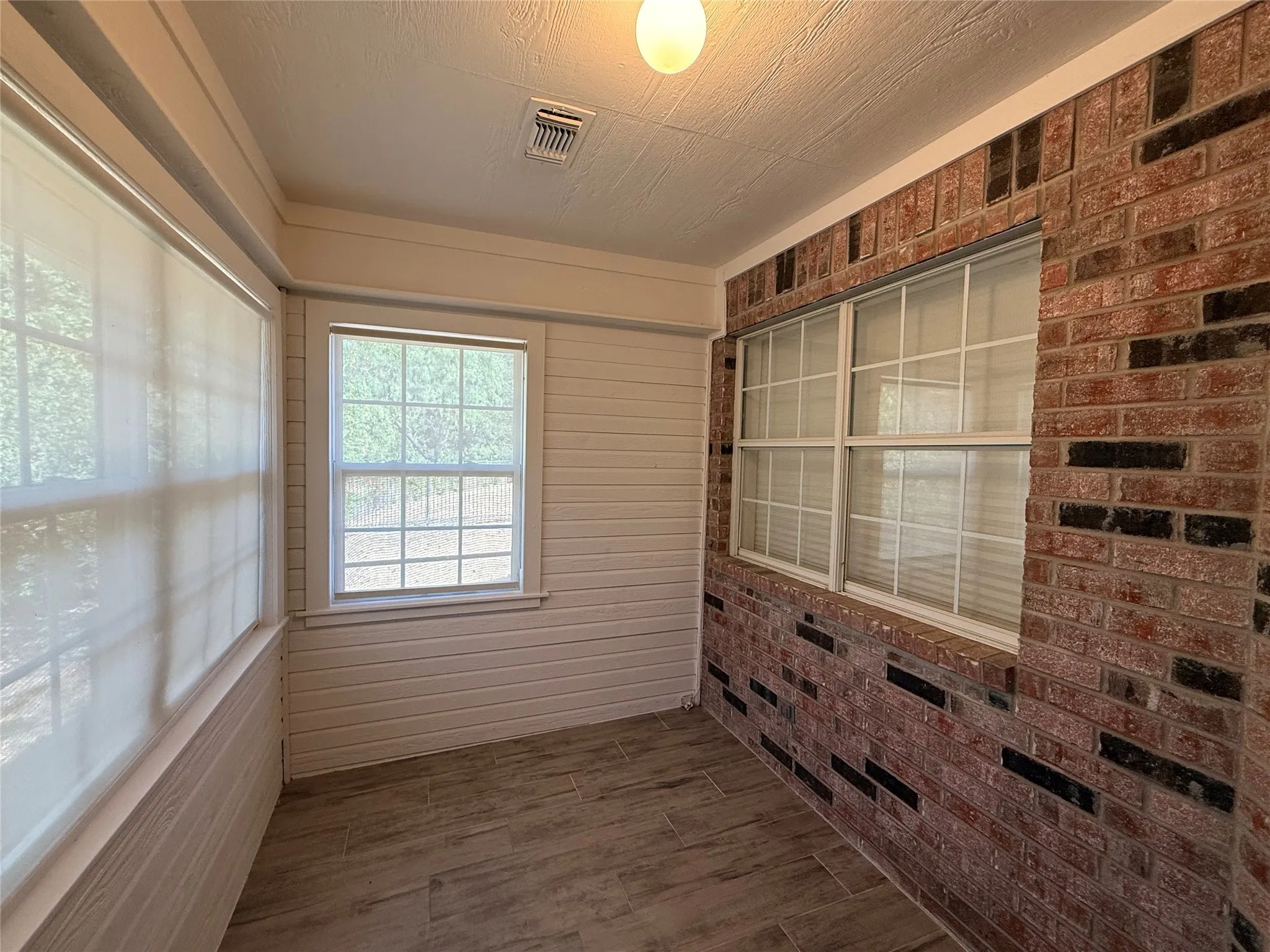 Enclosed room featuring exposed brick, wood-finish flooring, white horizontal paneling, and multiple grid-pattern windows