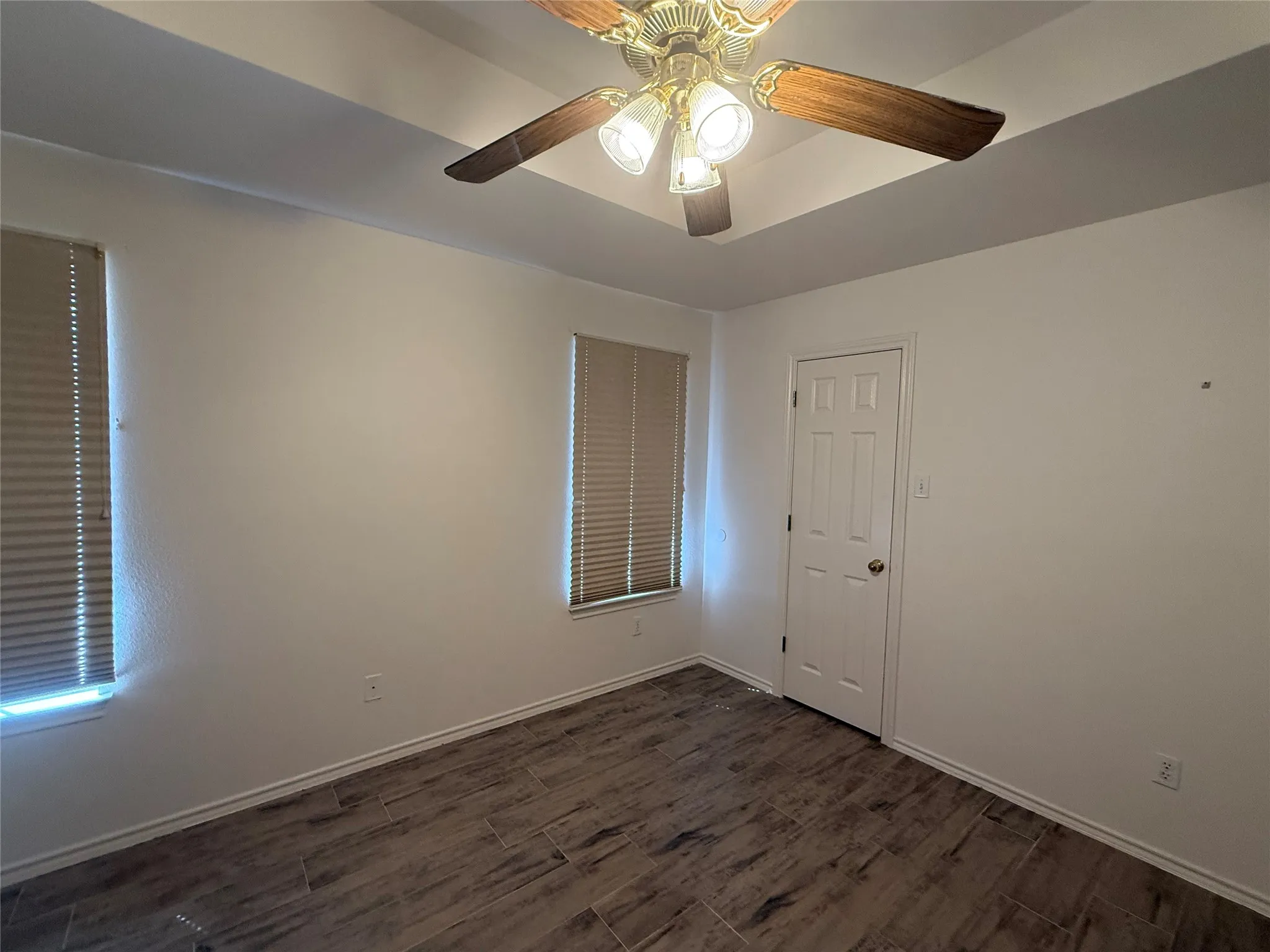 Tray ceiling with a decorative ceiling fan, wood-finish flooring, and two windows with blinds