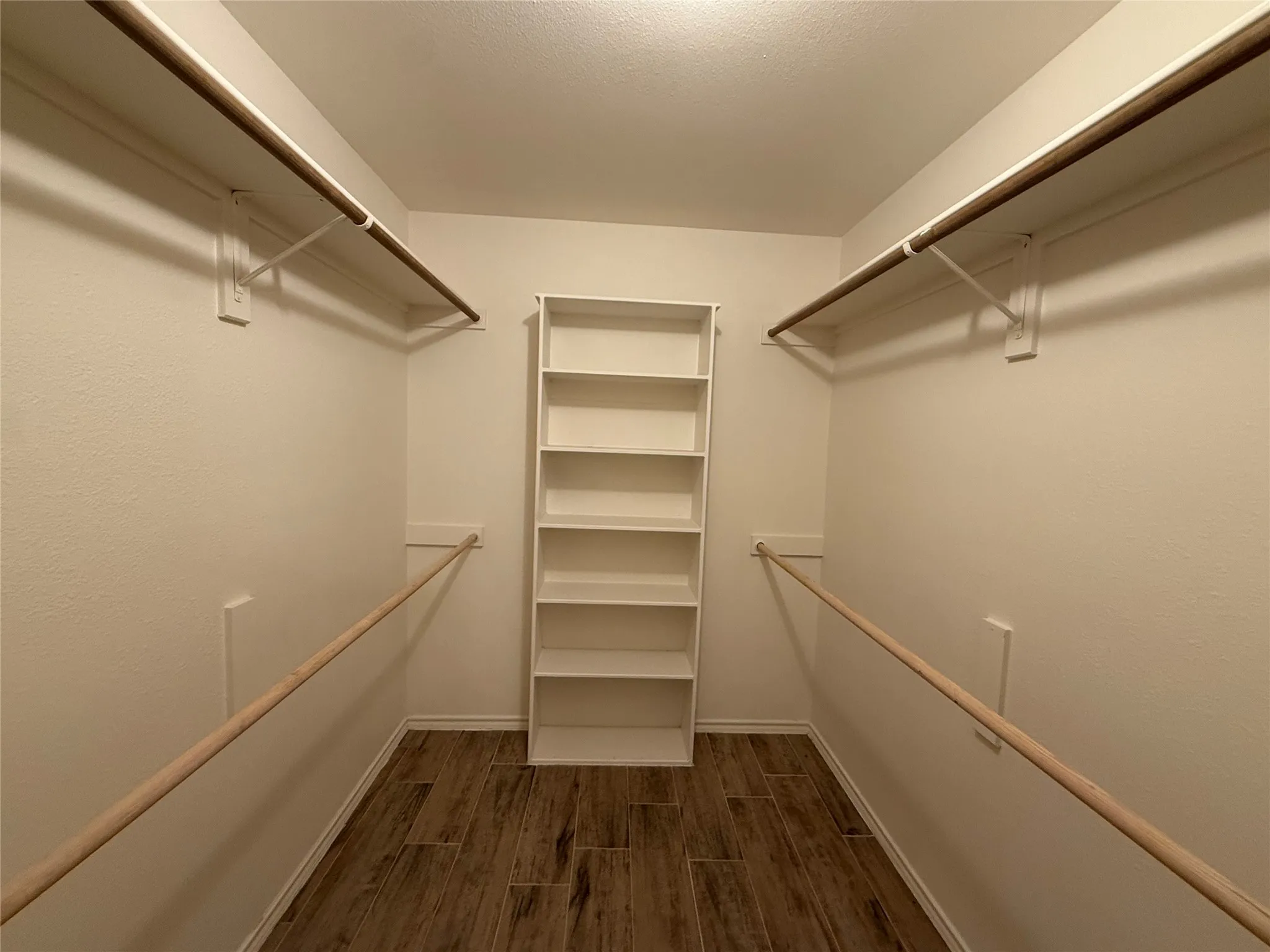 Walk-in closet featuring wood-finish flooring, built-in shelving, and multiple hanging rods