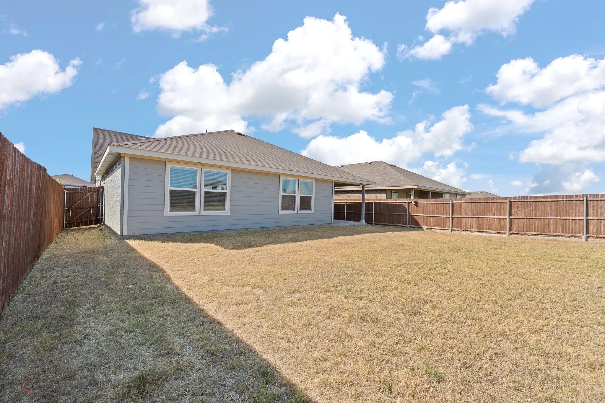 Fenced backyard with a covered patio, multiple windows, and a side gate