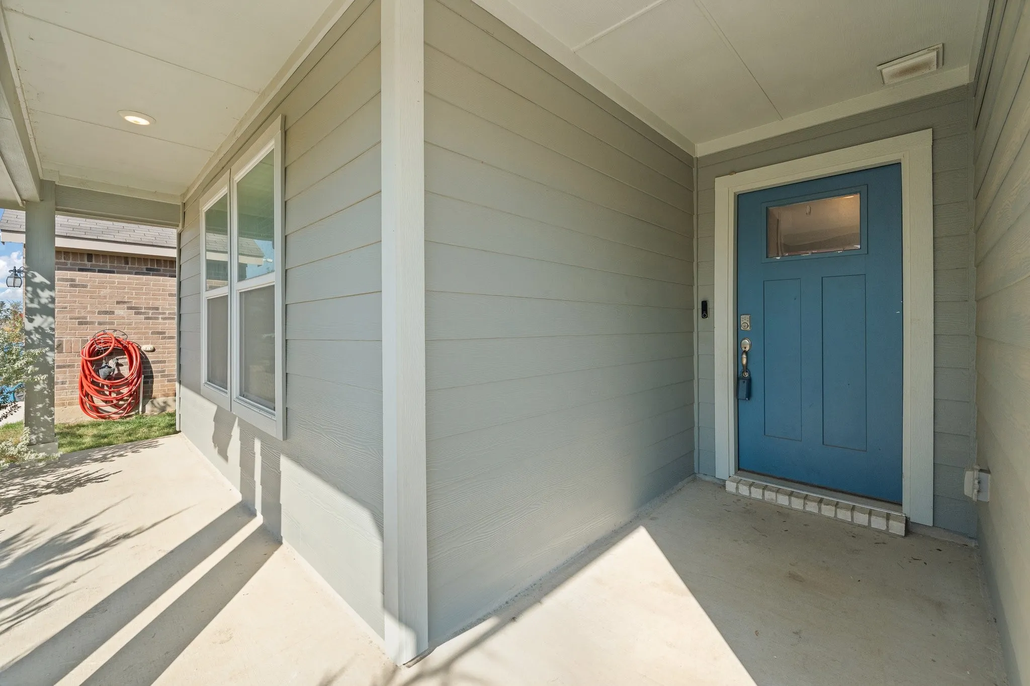 Covered front porch featuring a blue entry door with a window pane, light gray siding, and multiple windows