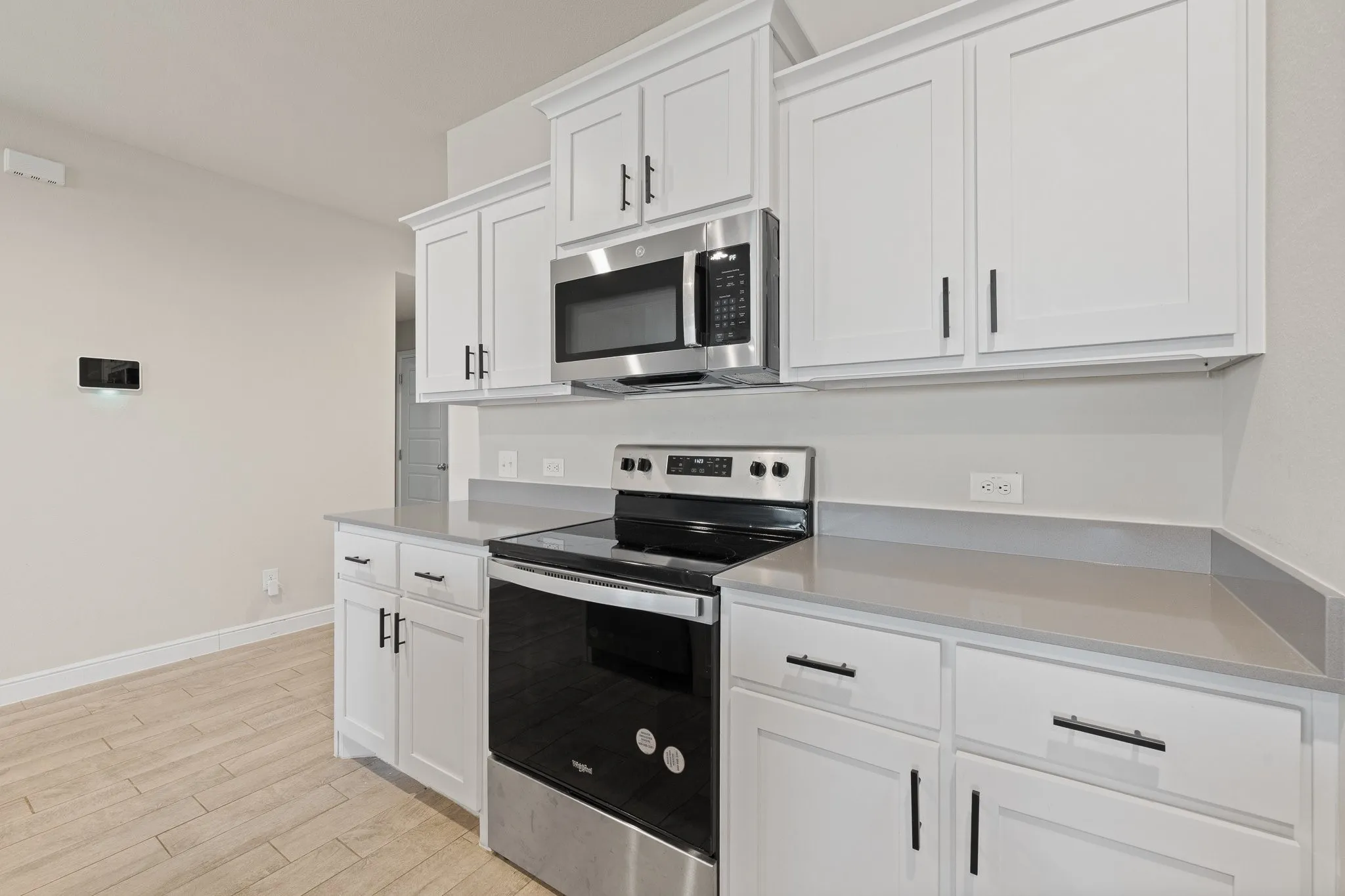 White shaker-style cabinetry with black hardware, stainless steel range, stainless steel microwave, light-toned countertops, and wood-finish tile flooring
