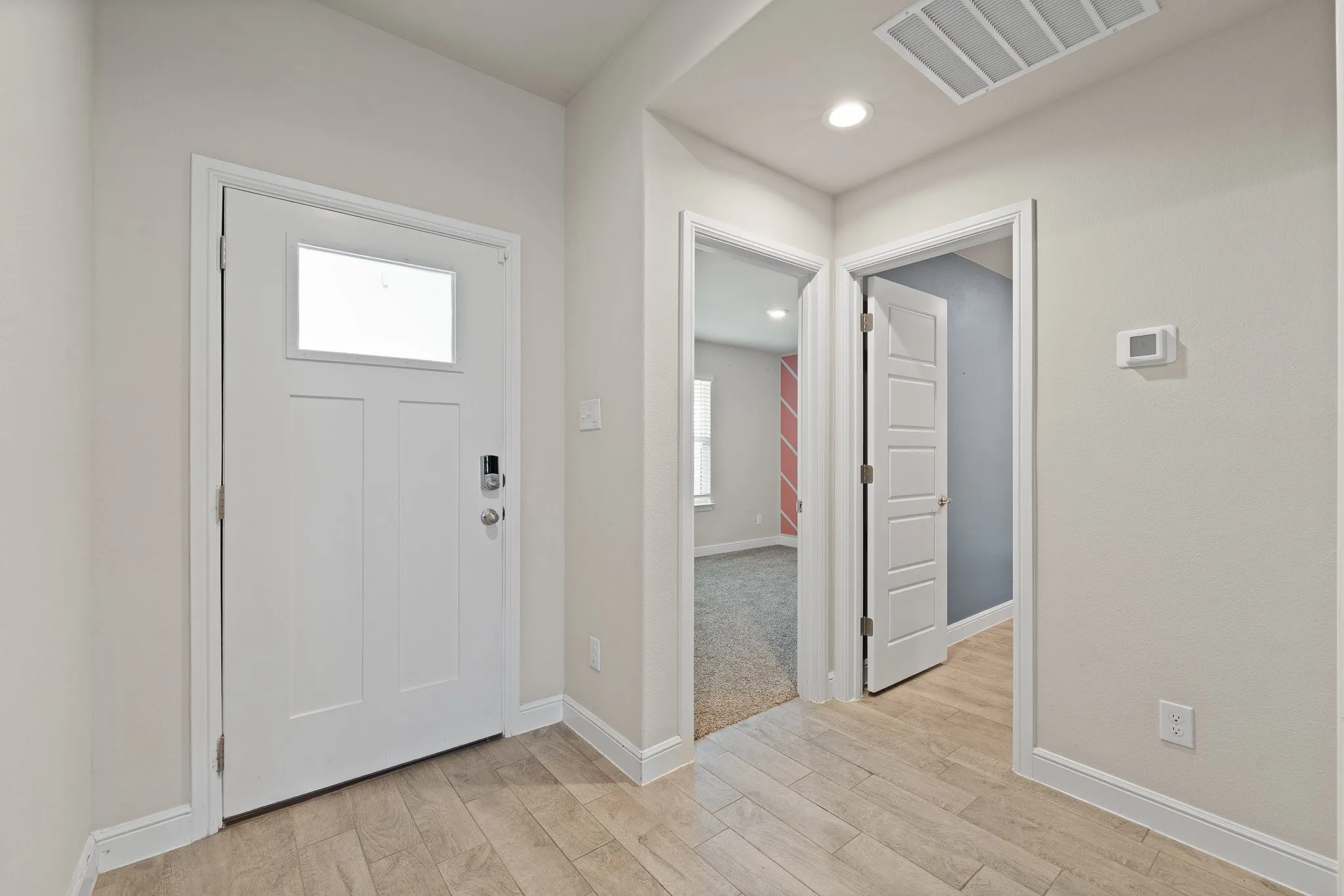 Entryway featuring a white paneled door with an upper window, wood-finish flooring, recessed lighting, and a digital thermostat