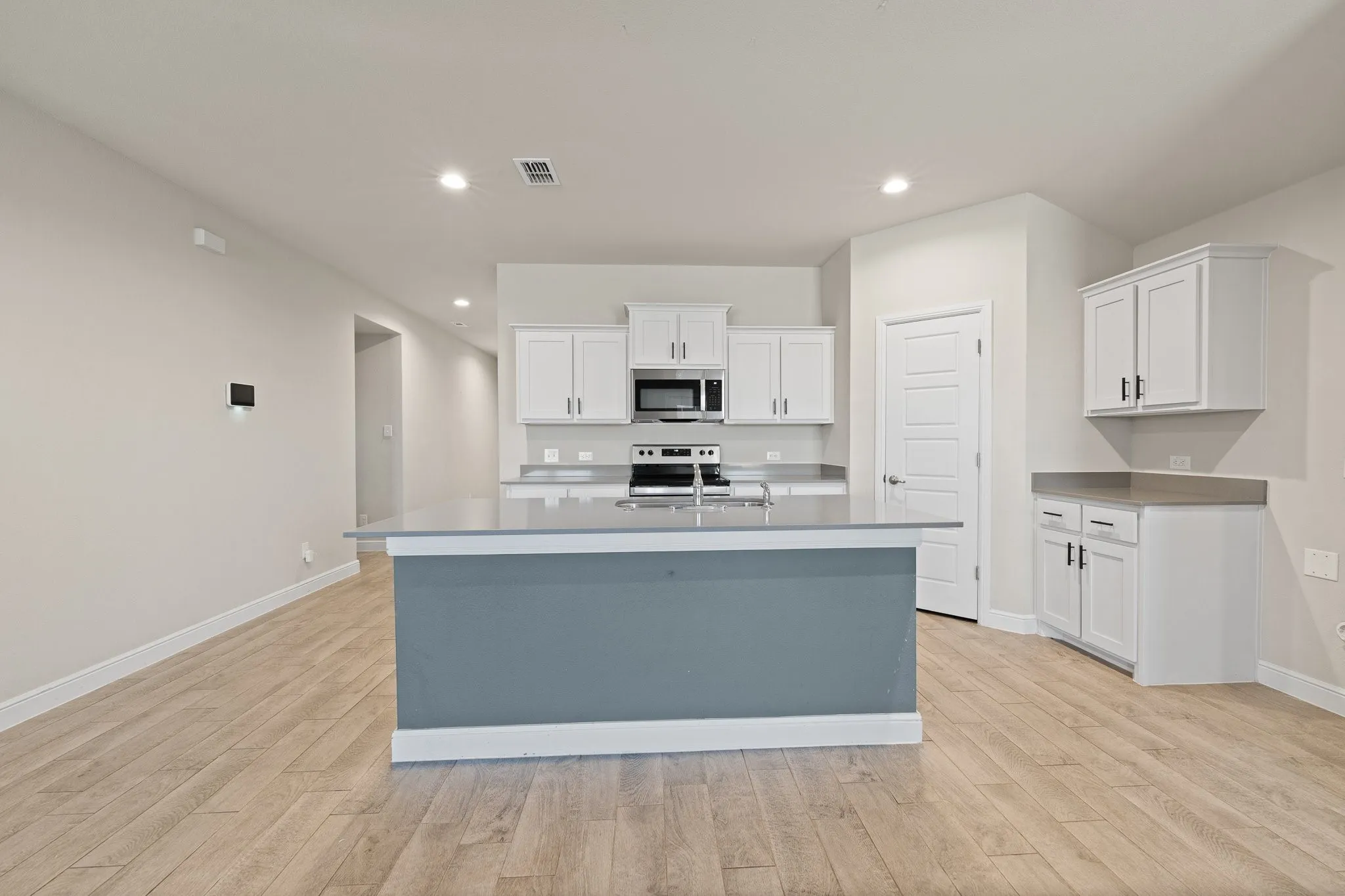 Open-concept kitchen with a central island, white cabinetry, integrated stainless steel appliances, and wood-finish flooring