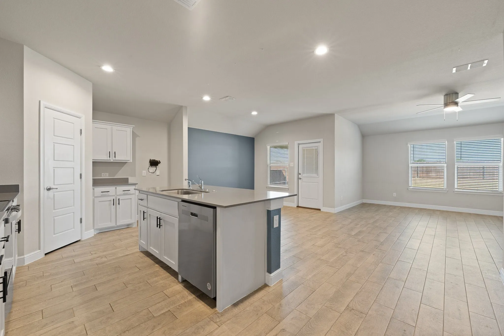 Open-concept layout featuring wood-finish tile flooring, a kitchen island with integrated sink and dishwasher, white cabinetry, and recessed lighting