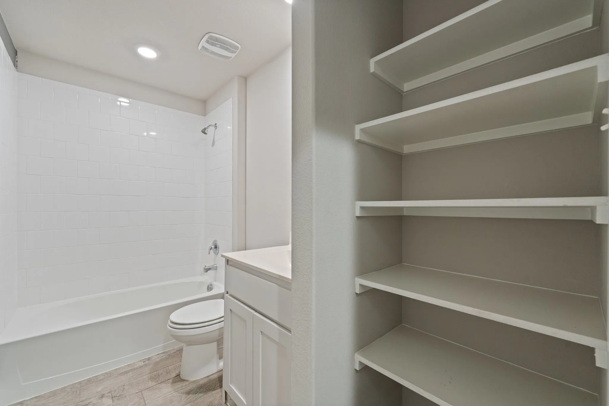 Built-in shelving, white subway tile shower surround, white vanity with countertop, wood-finish flooring, and recessed lighting
