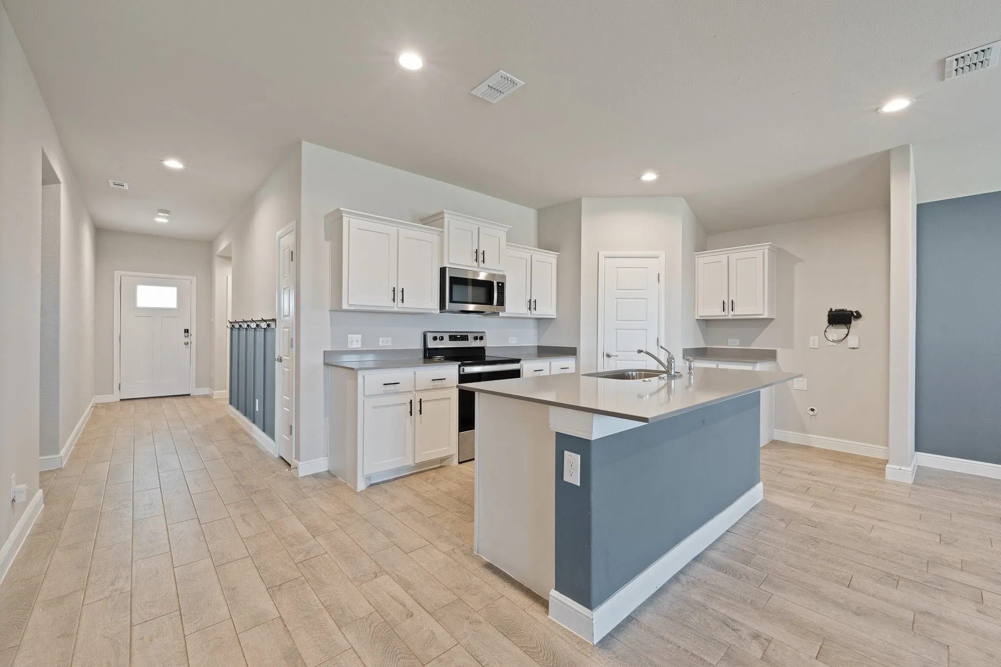 Open-concept kitchen with white cabinetry, stainless steel appliances, a center island featuring an undermount sink, and wood-finish flooring