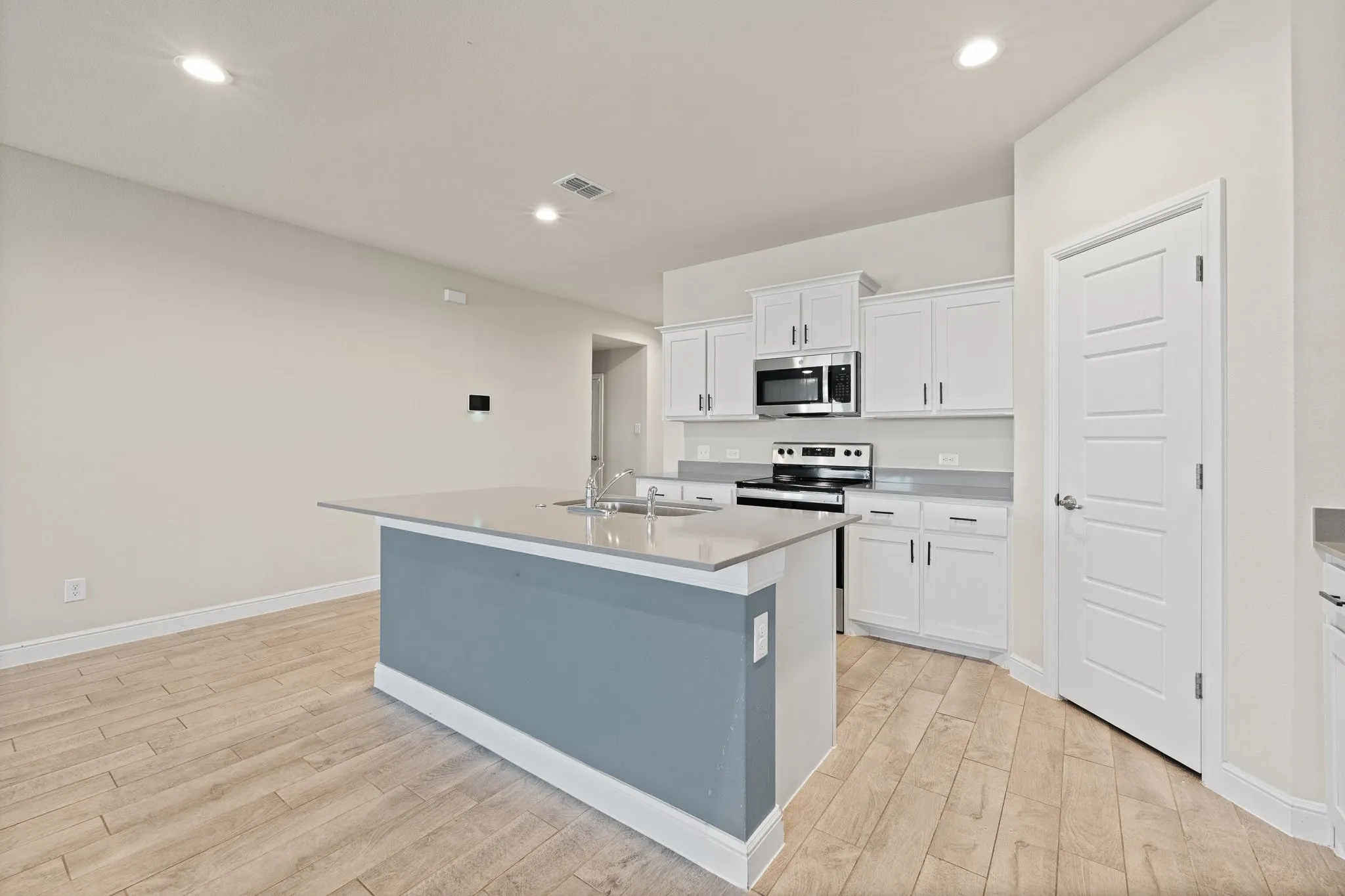 Well-appointed kitchen featuring white cabinetry, stainless steel appliances, a center island with sink, ample counter space, and wood-finish flooring
