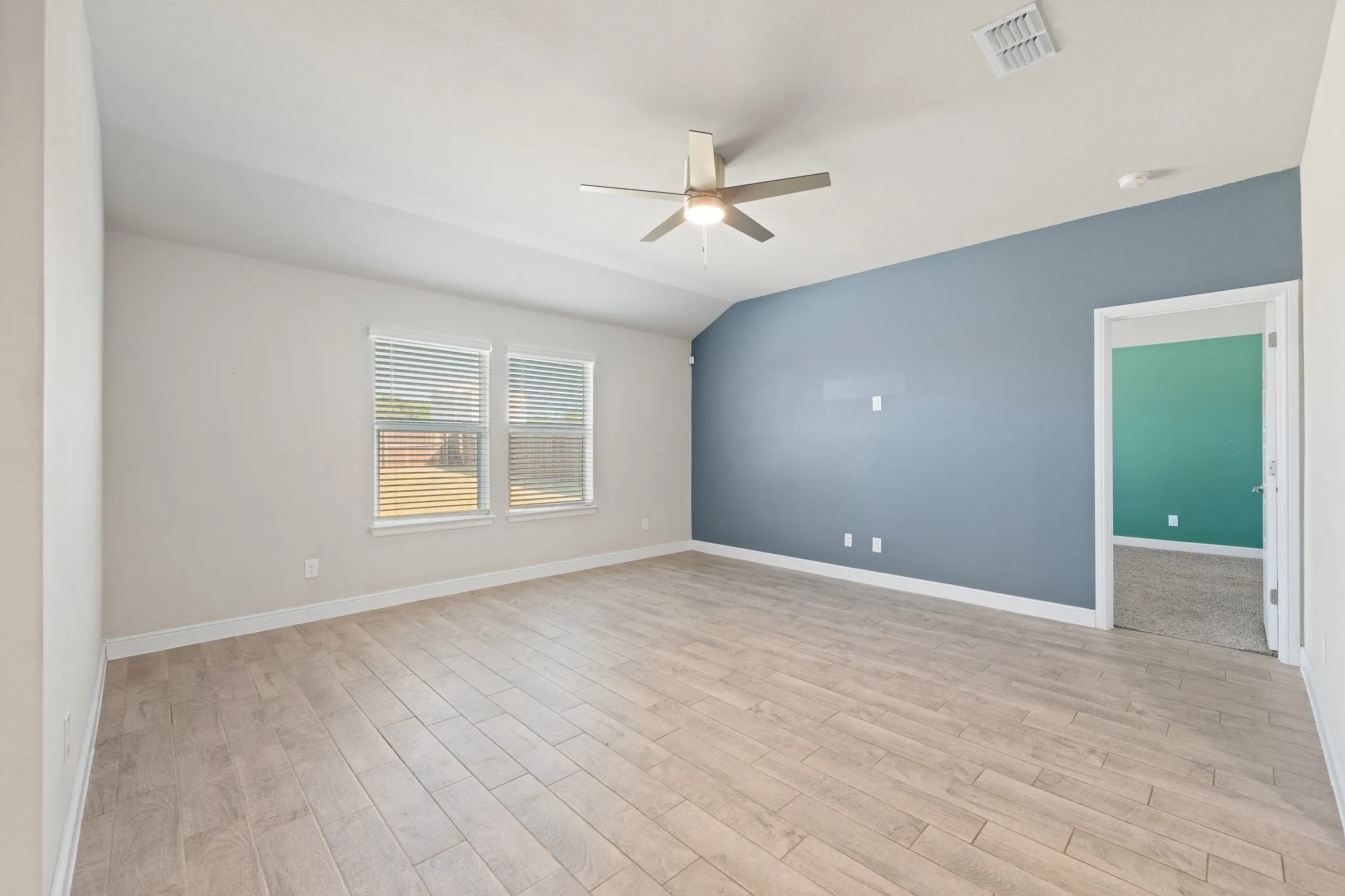 Vaulted ceiling with an attached ceiling fan, wood-finish flooring, and two windows