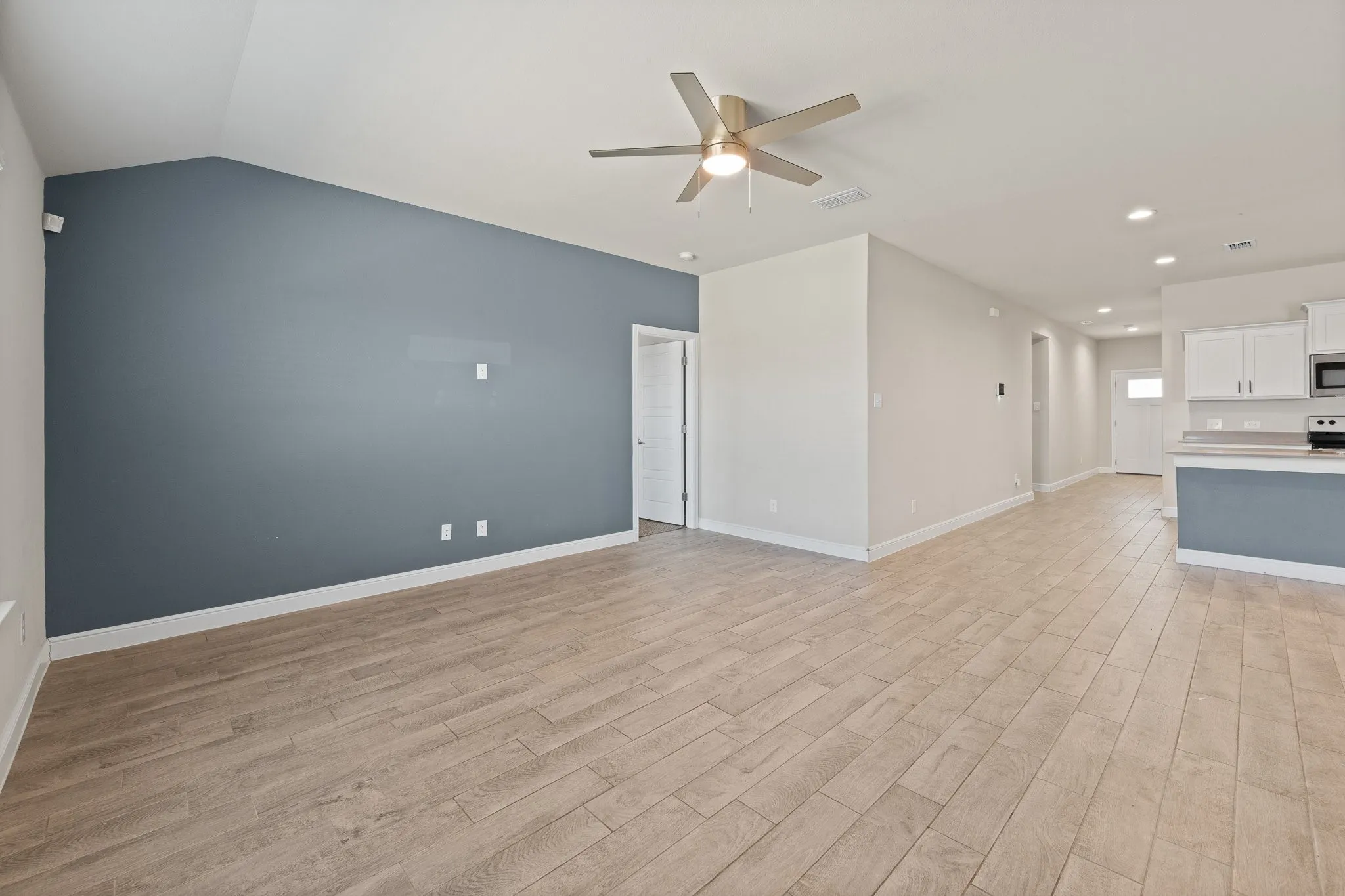 Vaulted ceiling with a ceiling fan, wood-finish flooring, recessed lighting, and a kitchen with white cabinetry