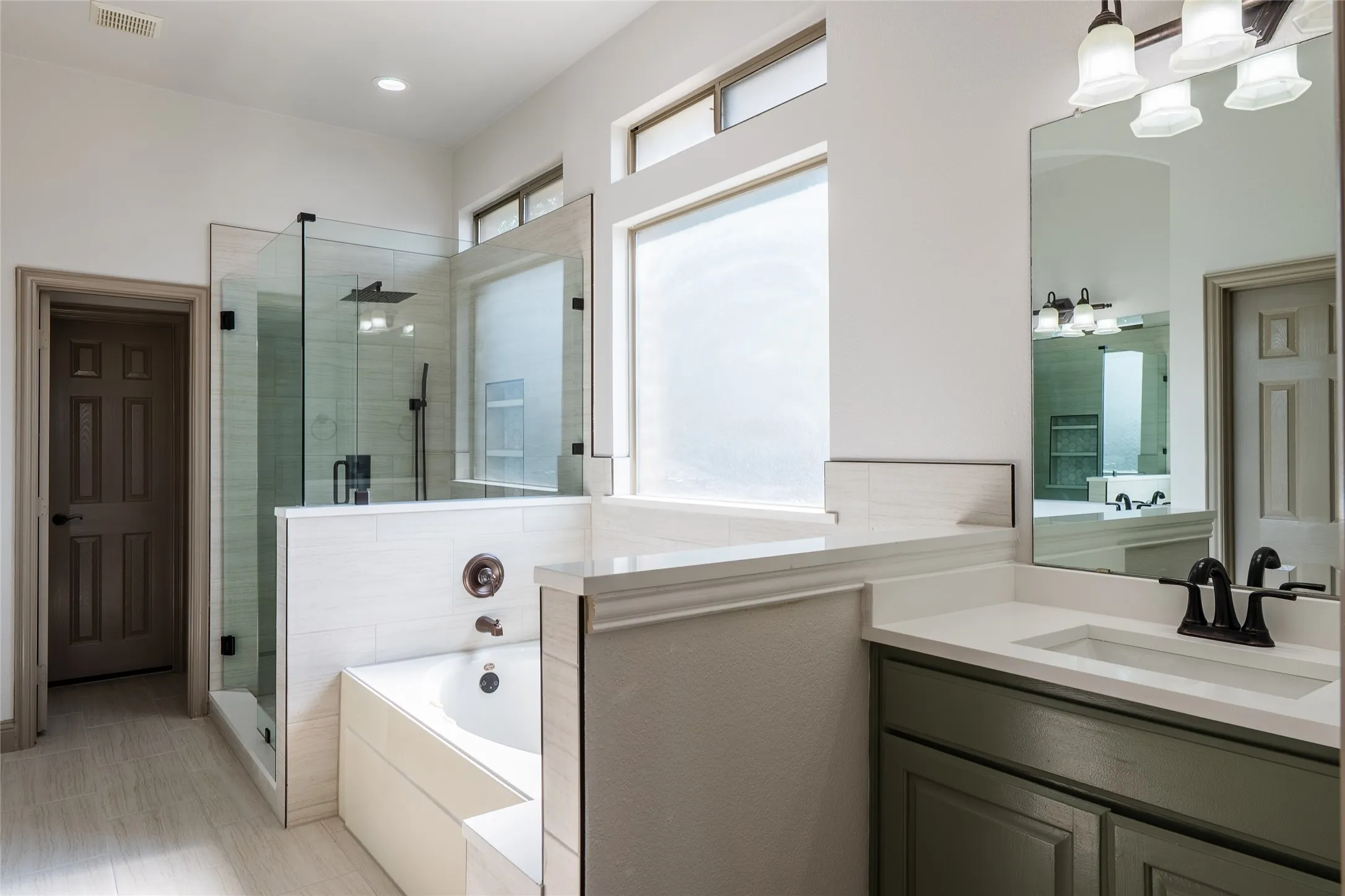 Walk-in glass shower with a rainfall showerhead, separate soaking tub, wood-finish flooring, single vanity with a solid surface countertop, and transom windows
