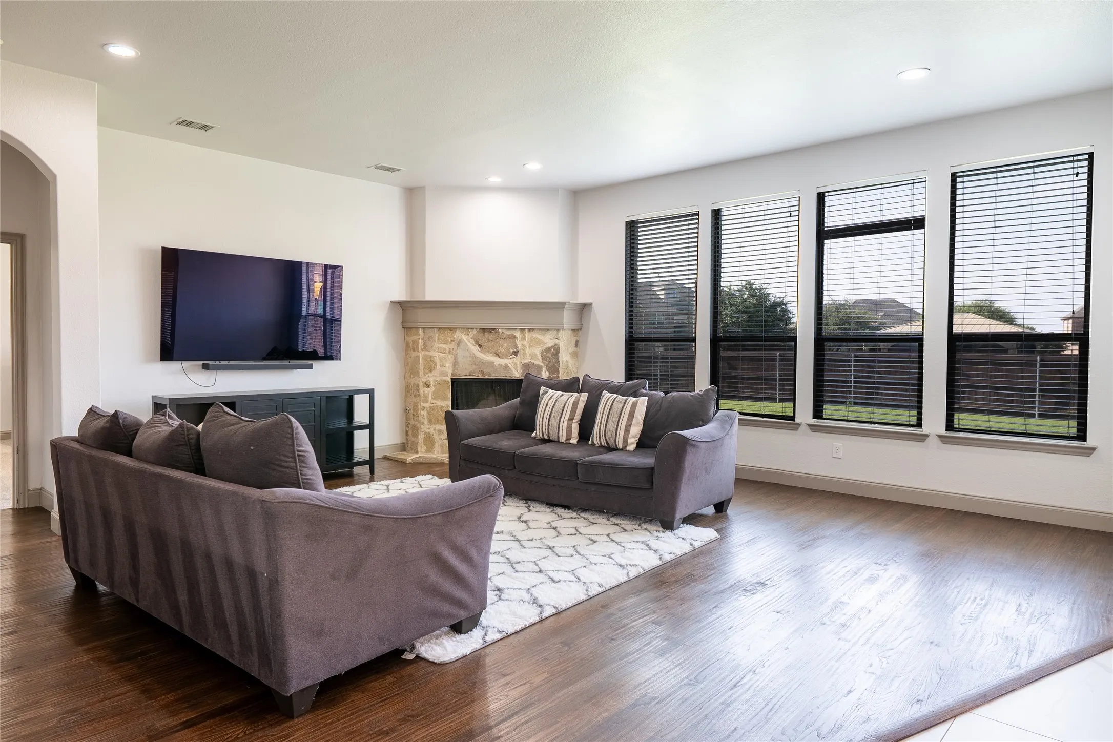 Hardwood flooring, recessed lighting, stone fireplace, multiple large windows, and a built-in media console