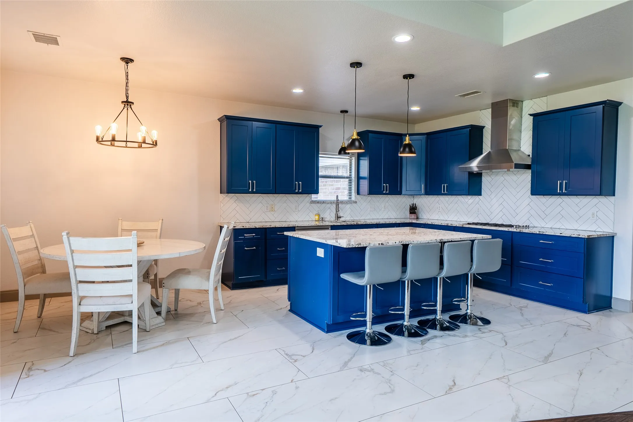 Kitchen featuring blue cabinetry, a stainless steel range hood, pendant lighting, white subway tile backsplash, and an island with bar seating