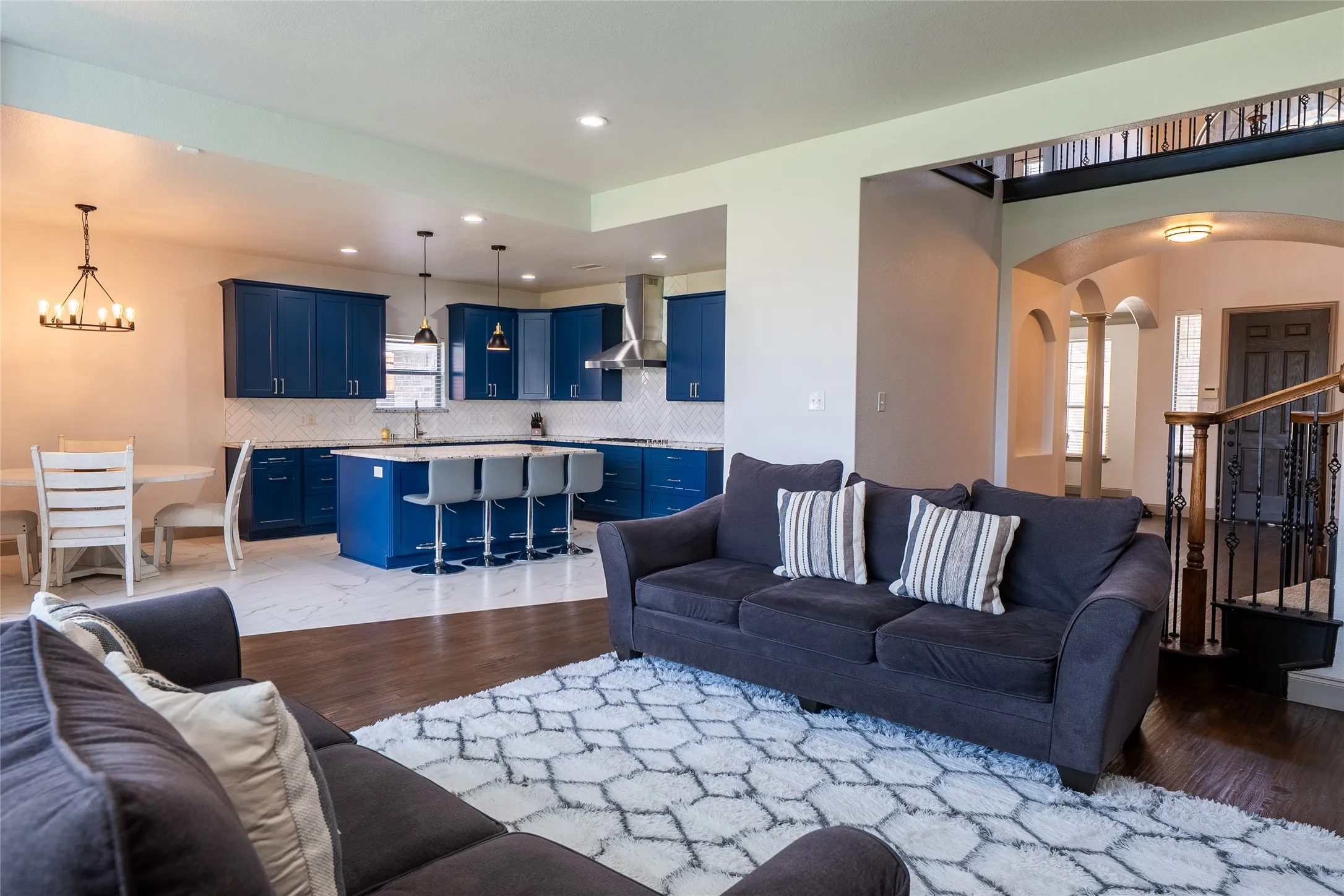 Open-concept living space with dark wood-finish flooring, a kitchen featuring blue cabinetry and an island, a tiled kitchen floor, and a staircase with an ornamental railing