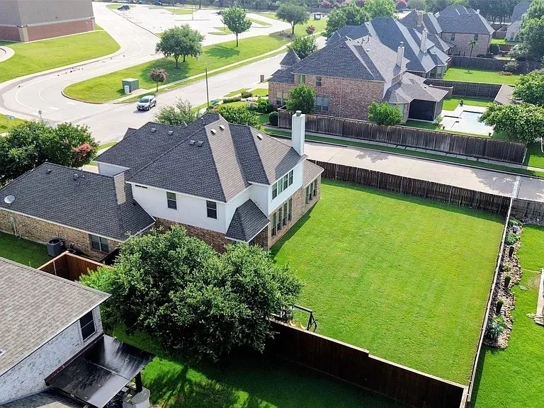 Expansive backyard featuring a manicured lawn, full perimeter fencing, and mature trees