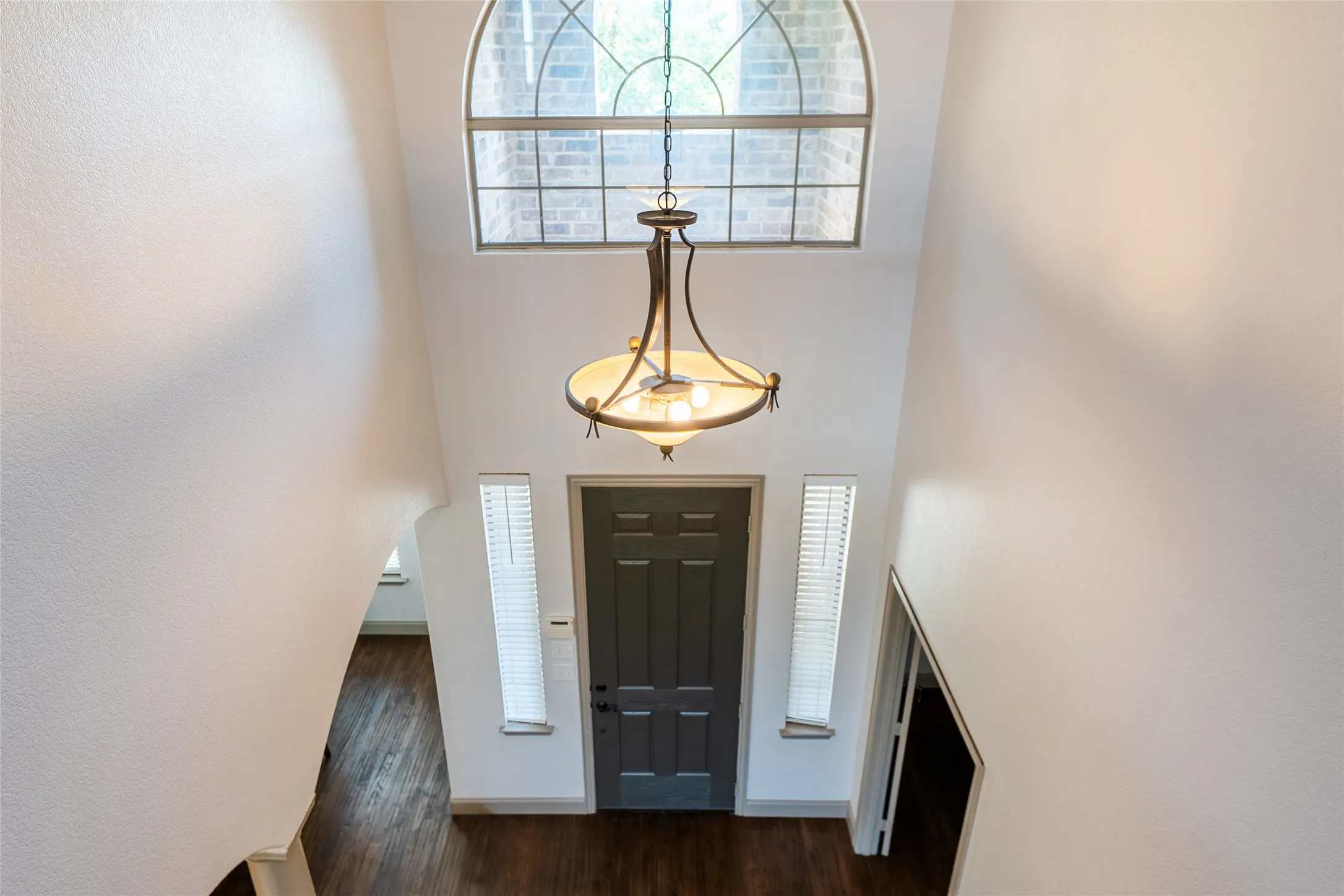Two-story entry featuring an arched window, dark wood-finish flooring, and a decorative chandelier