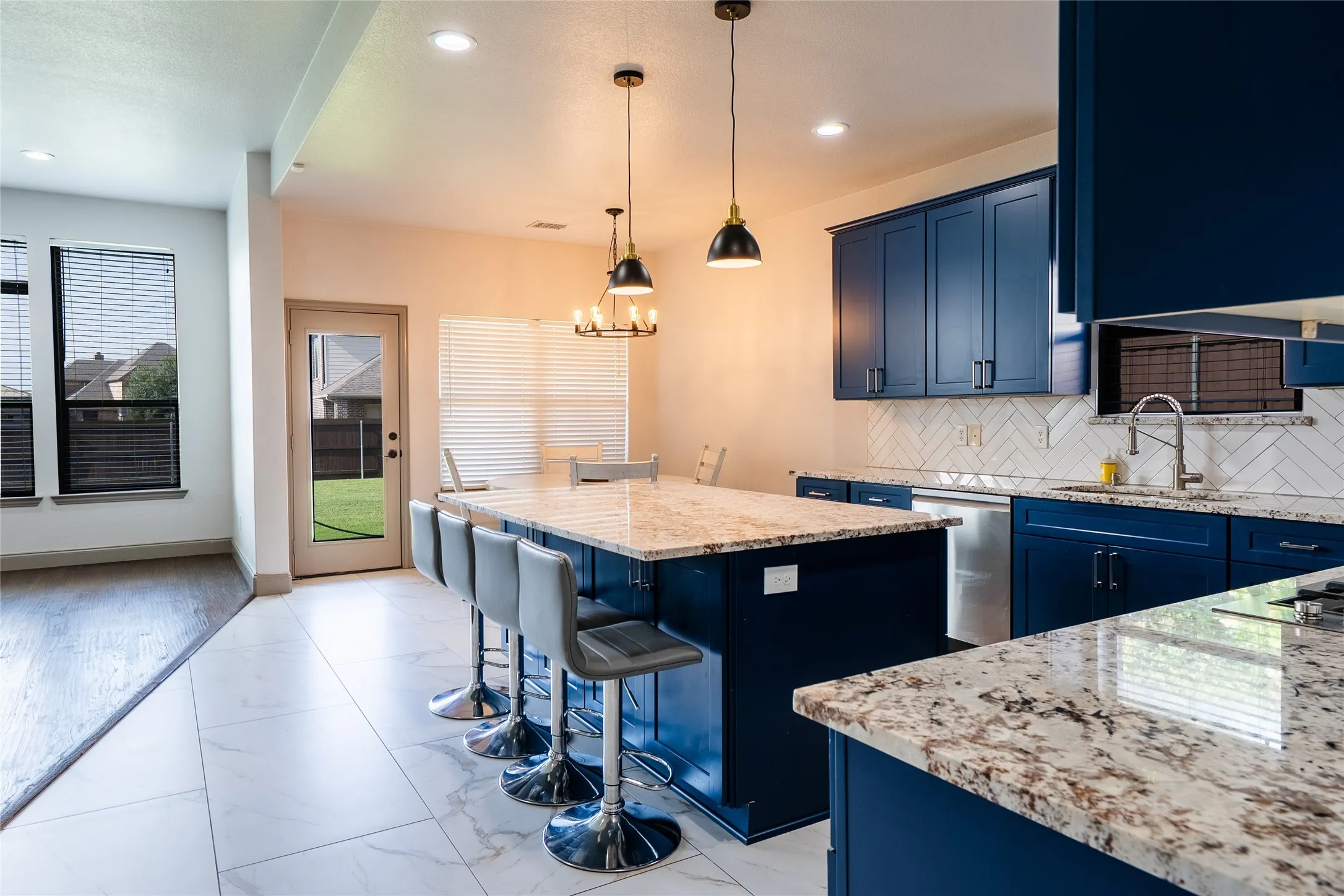 Kitchen featuring blue cabinetry, light-colored countertops, white tile backsplash, and an island with pendant lighting