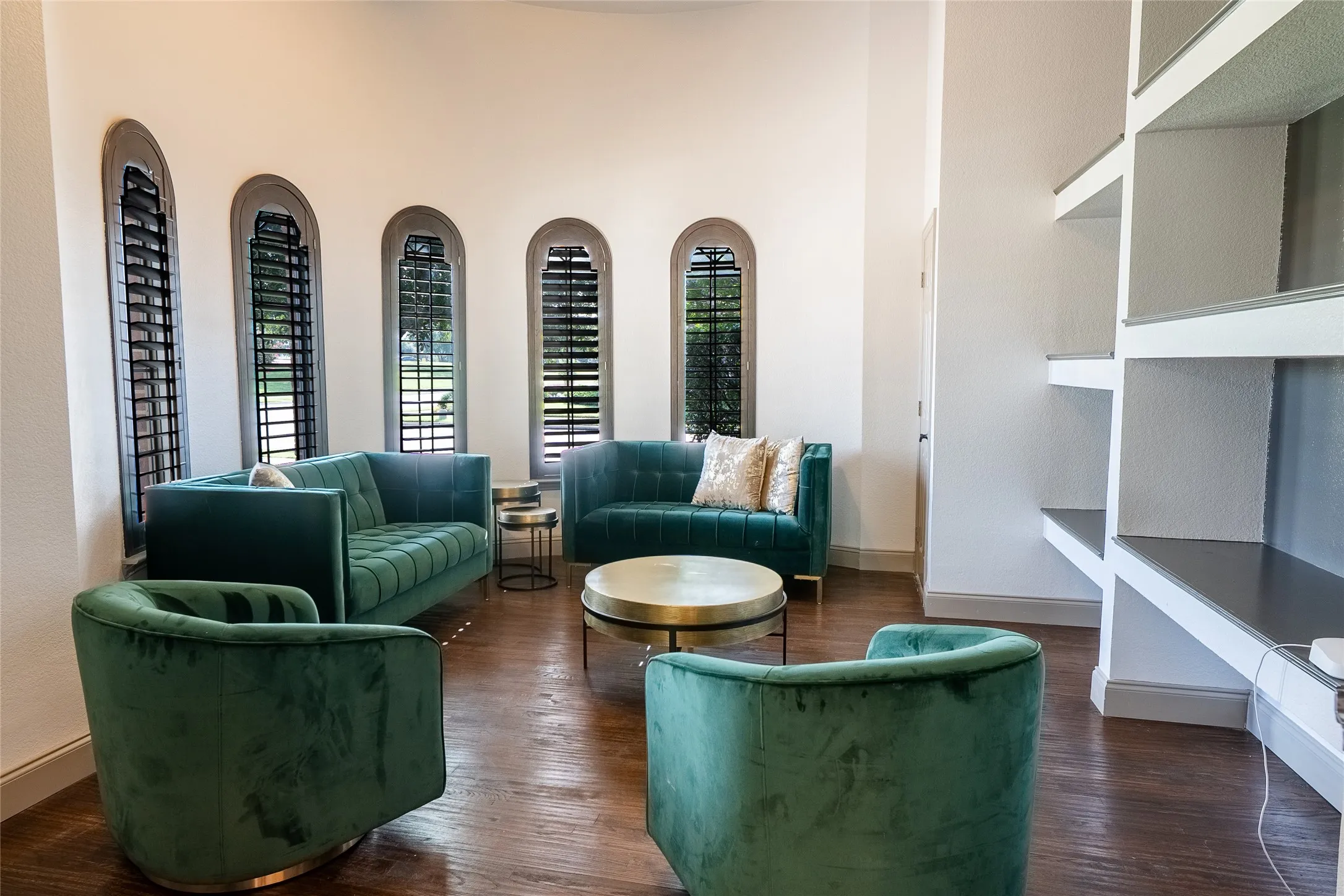 Room featuring arched windows with dark shutters, wood-finish flooring, and built-in shelving