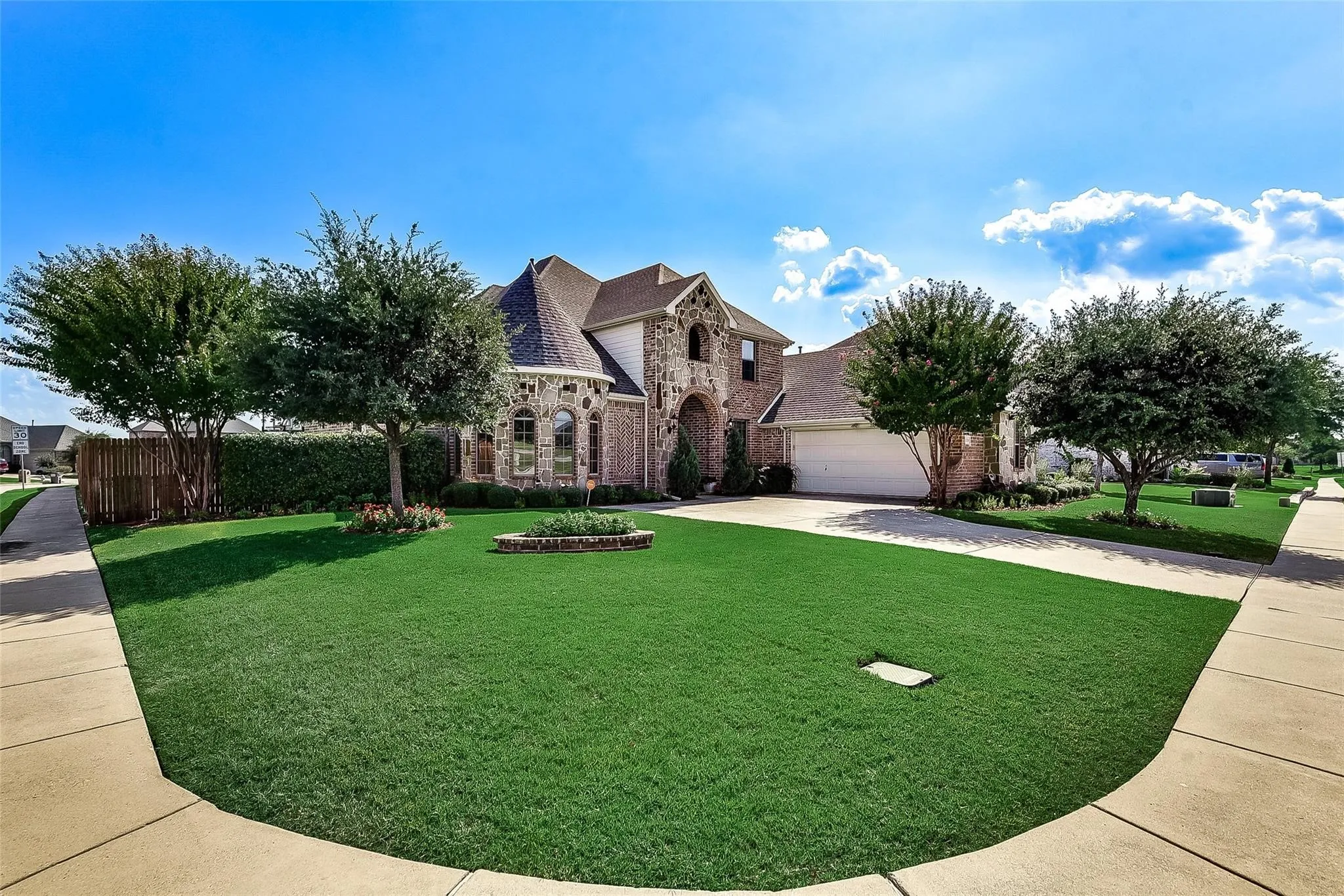 Brick and stone exterior with arched entryway, manicured lawn, mature trees, and an attached two-car garage