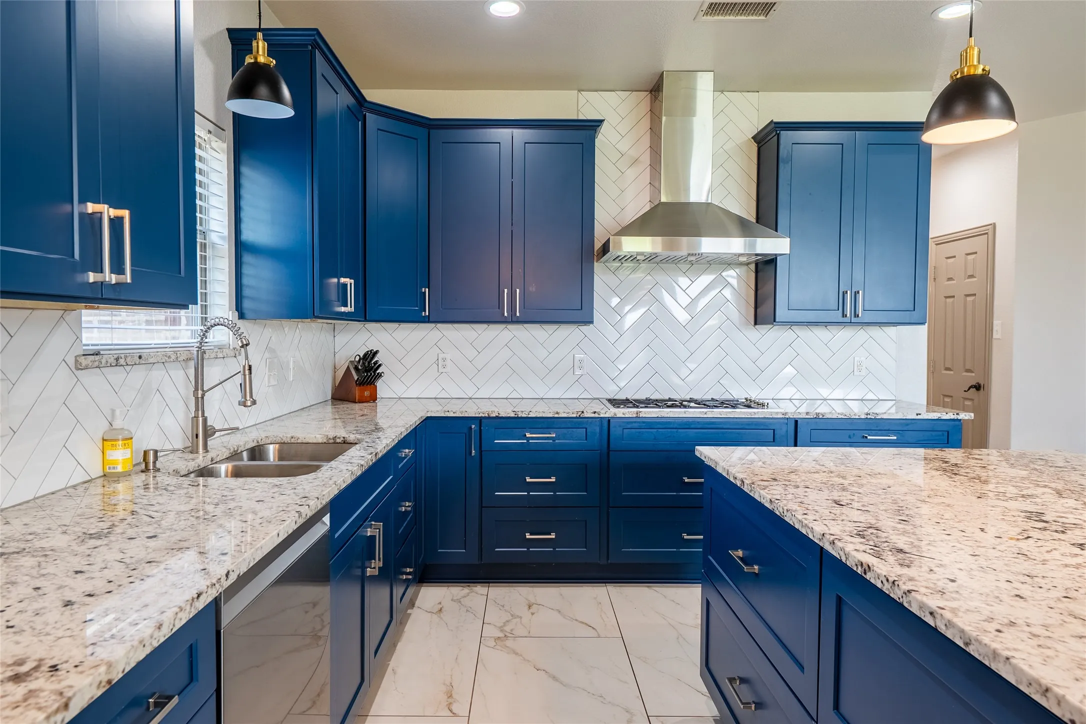 Full kitchen with blue cabinetry, light granite countertops, a herringbone tile backsplash, and a stainless steel range hood