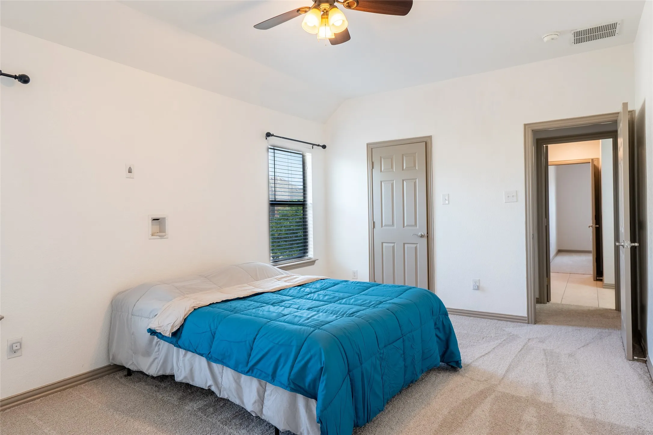 Carpeted flooring, window with blinds, ceiling fan with light fixture, and a paneled interior door